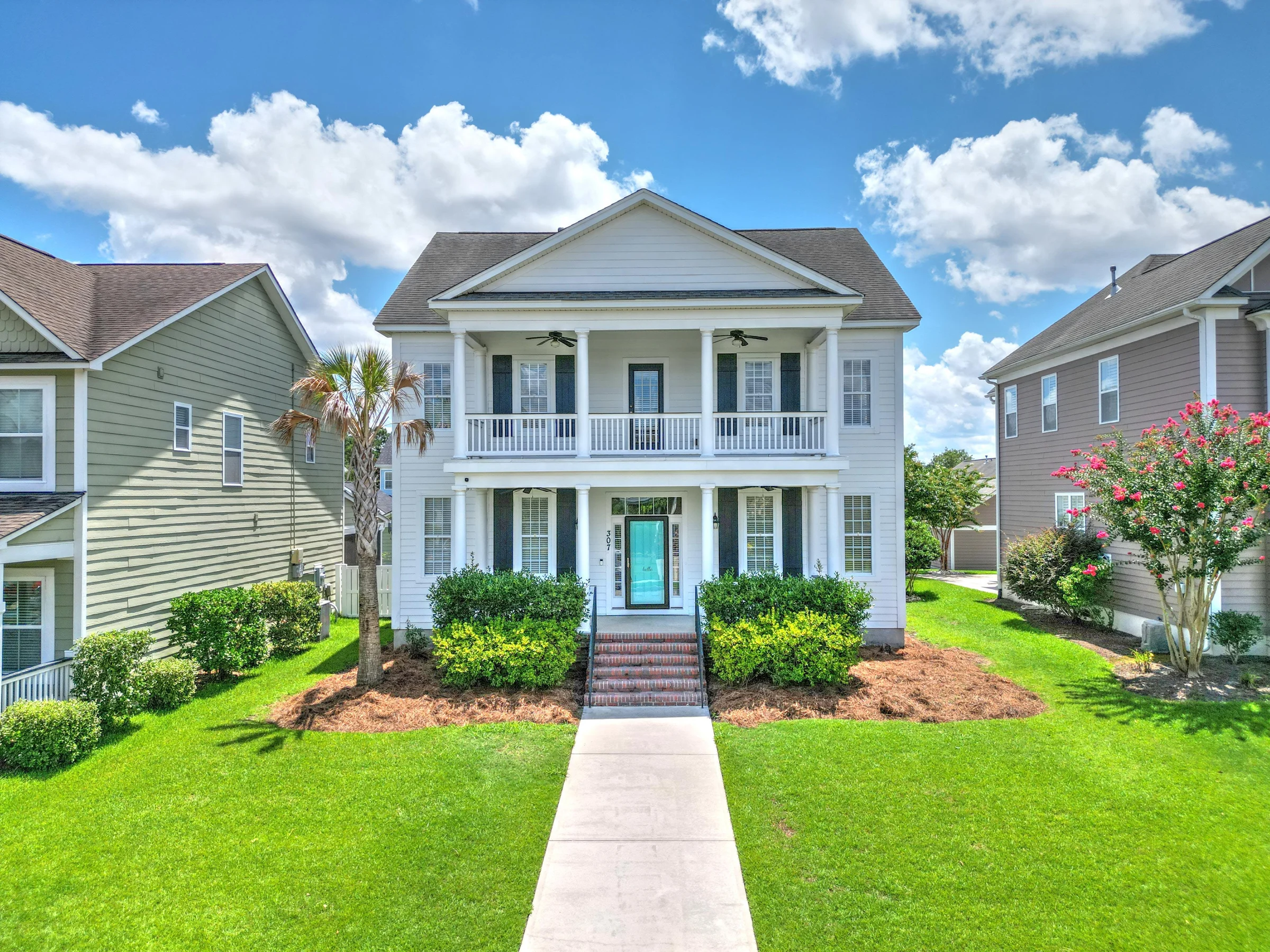 Two-story white home with a balcony, front porch, and landscaped lawn