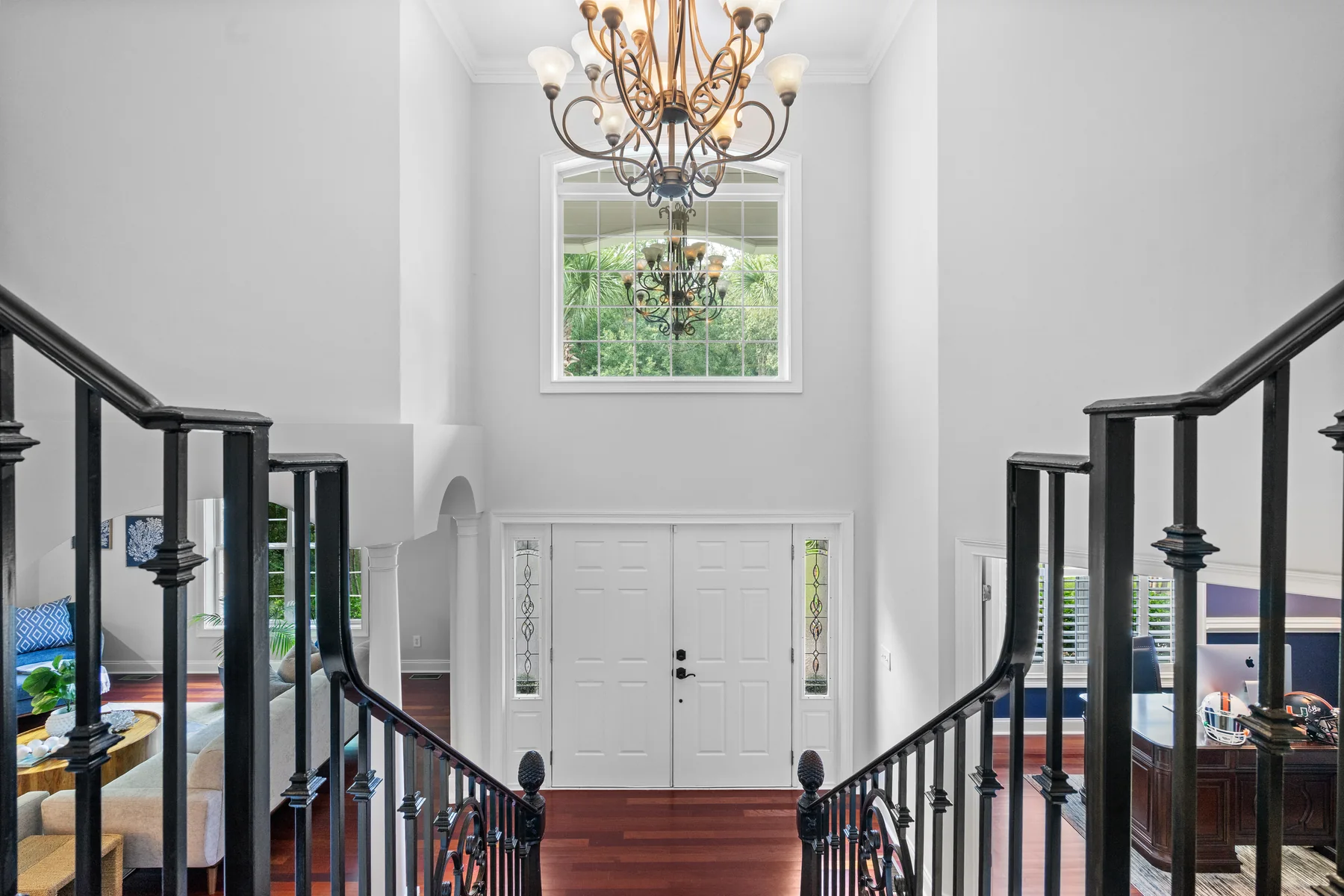 Staircase with black railings leading to a white front door beneath a chandelier