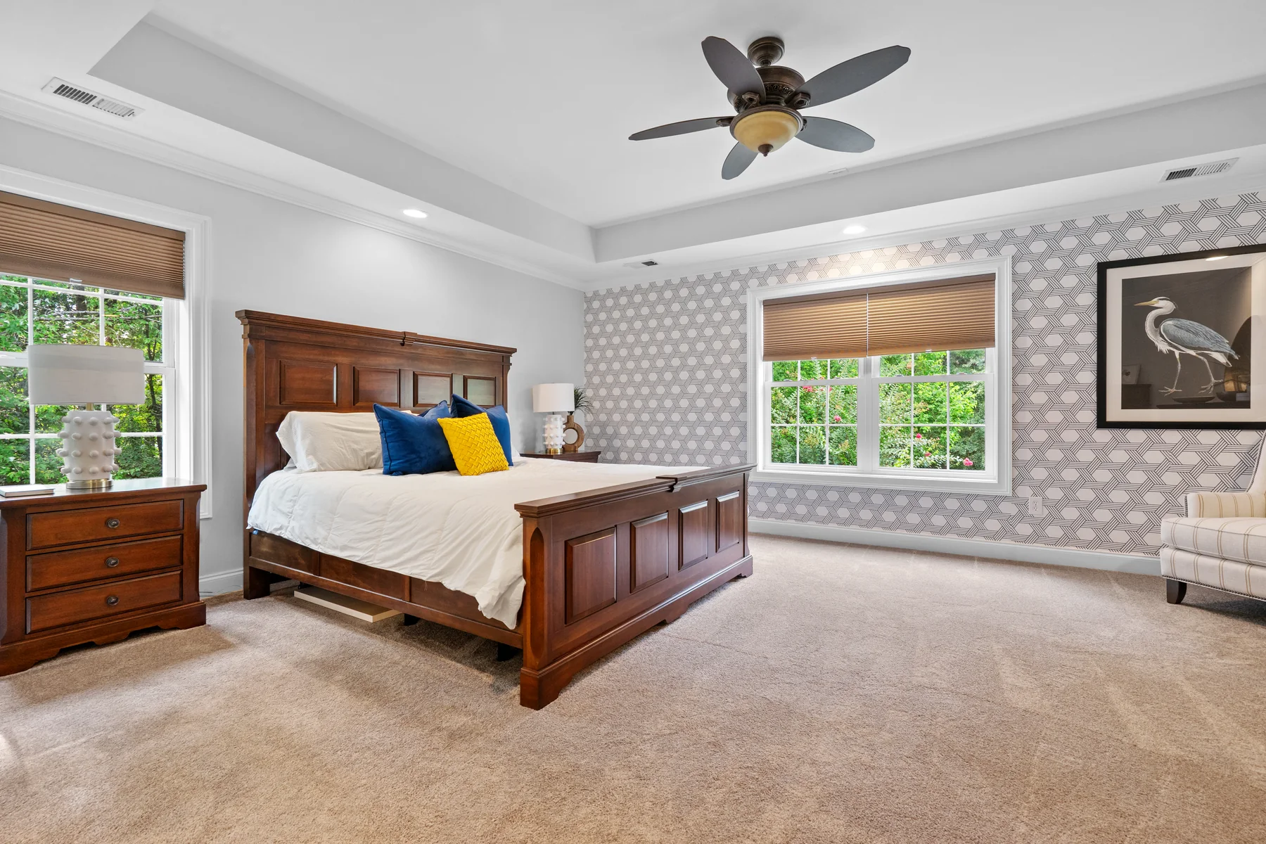 Bedroom with a wooden bed, patterned wallpaper, two windows, and a ceiling fan