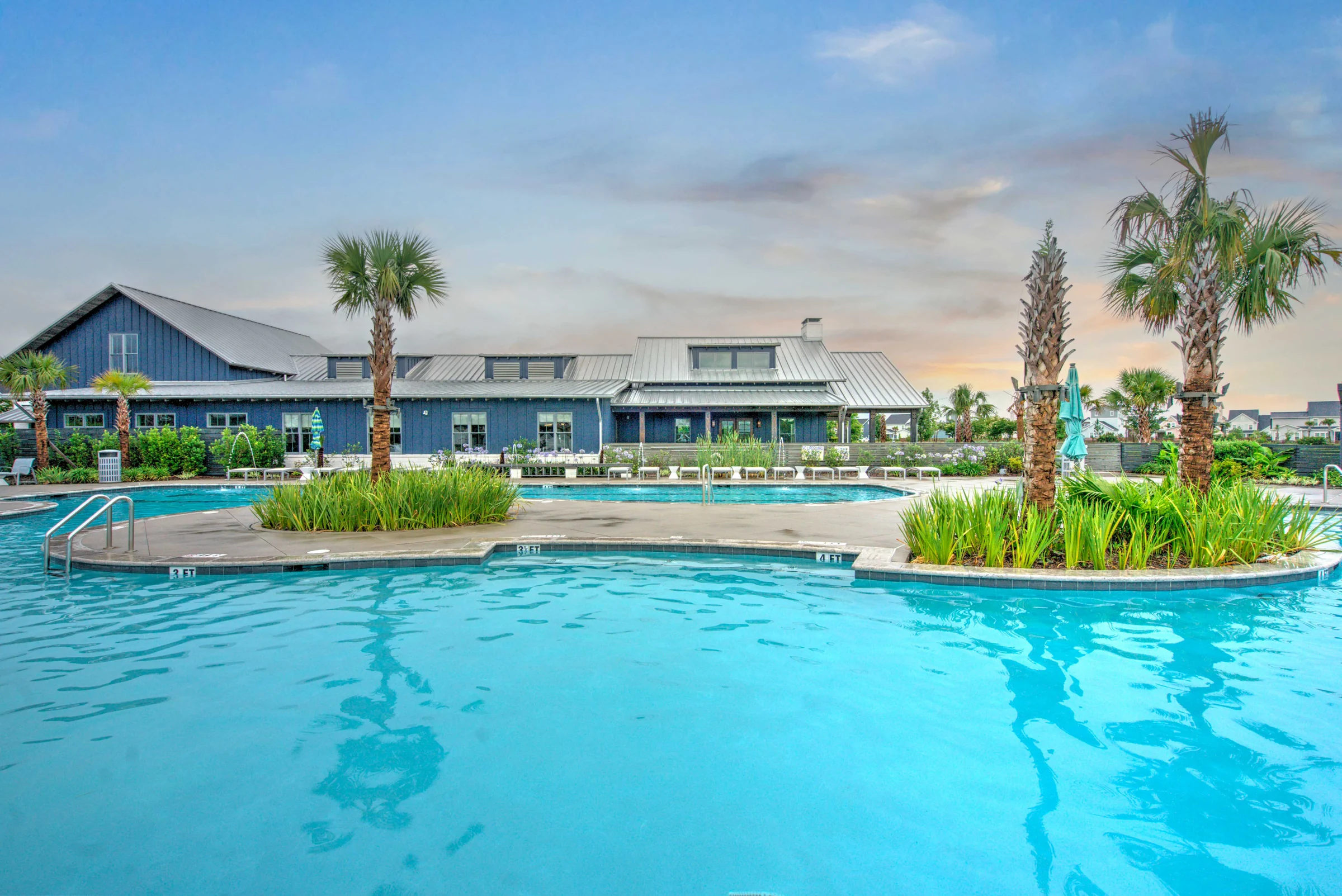Aerial drone photo of a blue amenity building with a metal roof beside a pool and palm trees