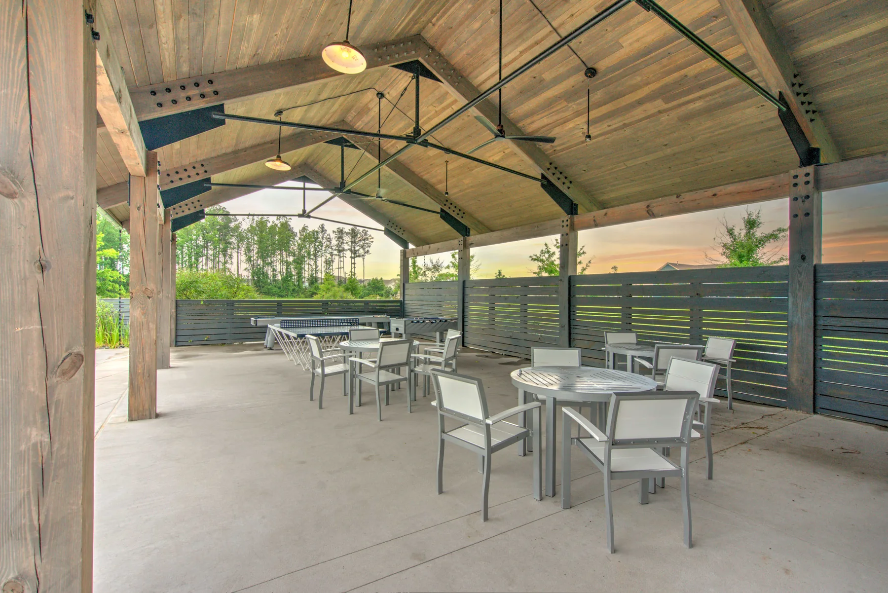 Covered patio pavilion with tables, chairs, wooden beams, and ceiling fans