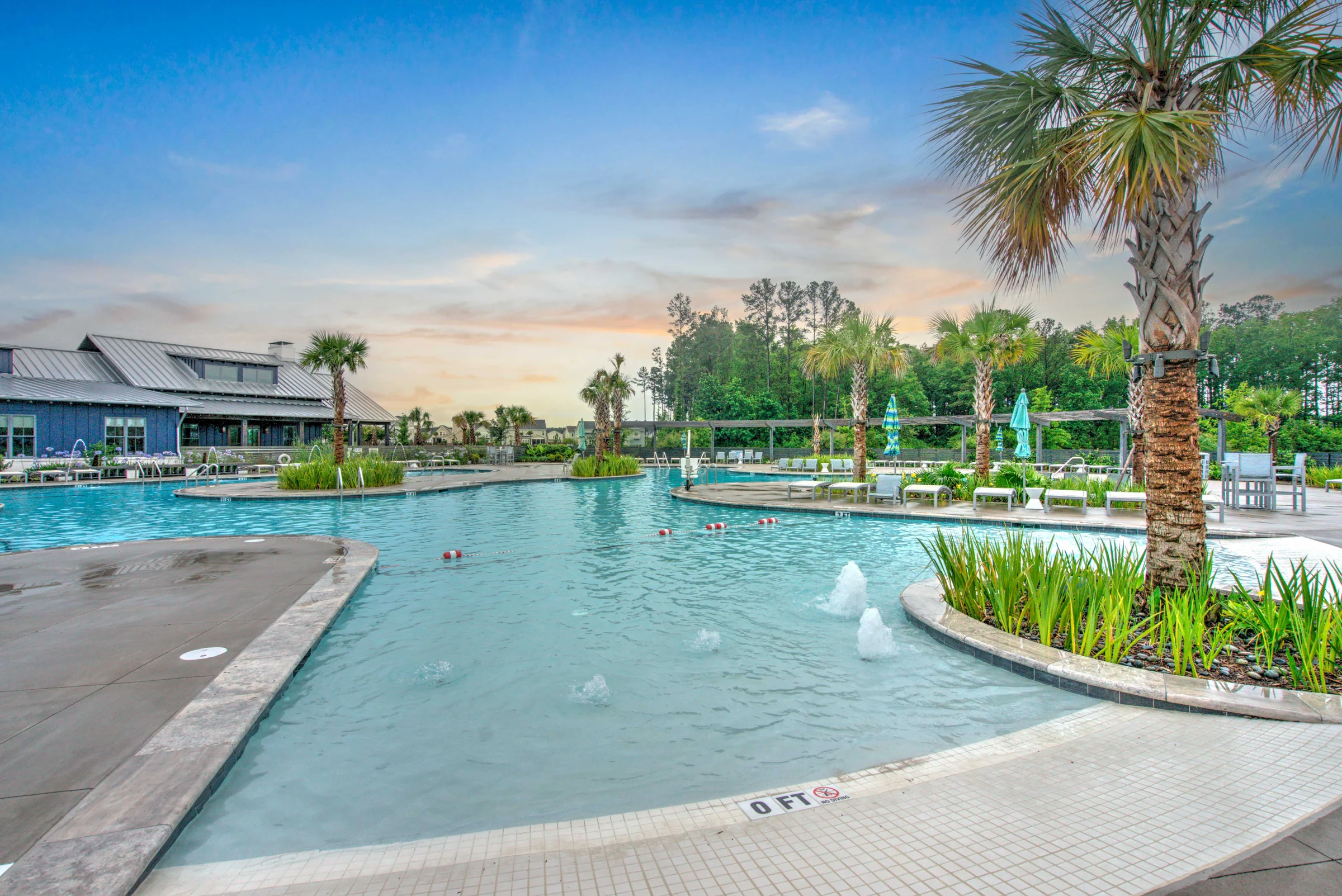 Aerial drone photo of a large swimming pool with palm trees and a clubhouse