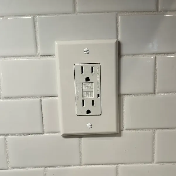 A real GFCI receptacle with TEST and RESET buttons in a tiled kitchen backsplash