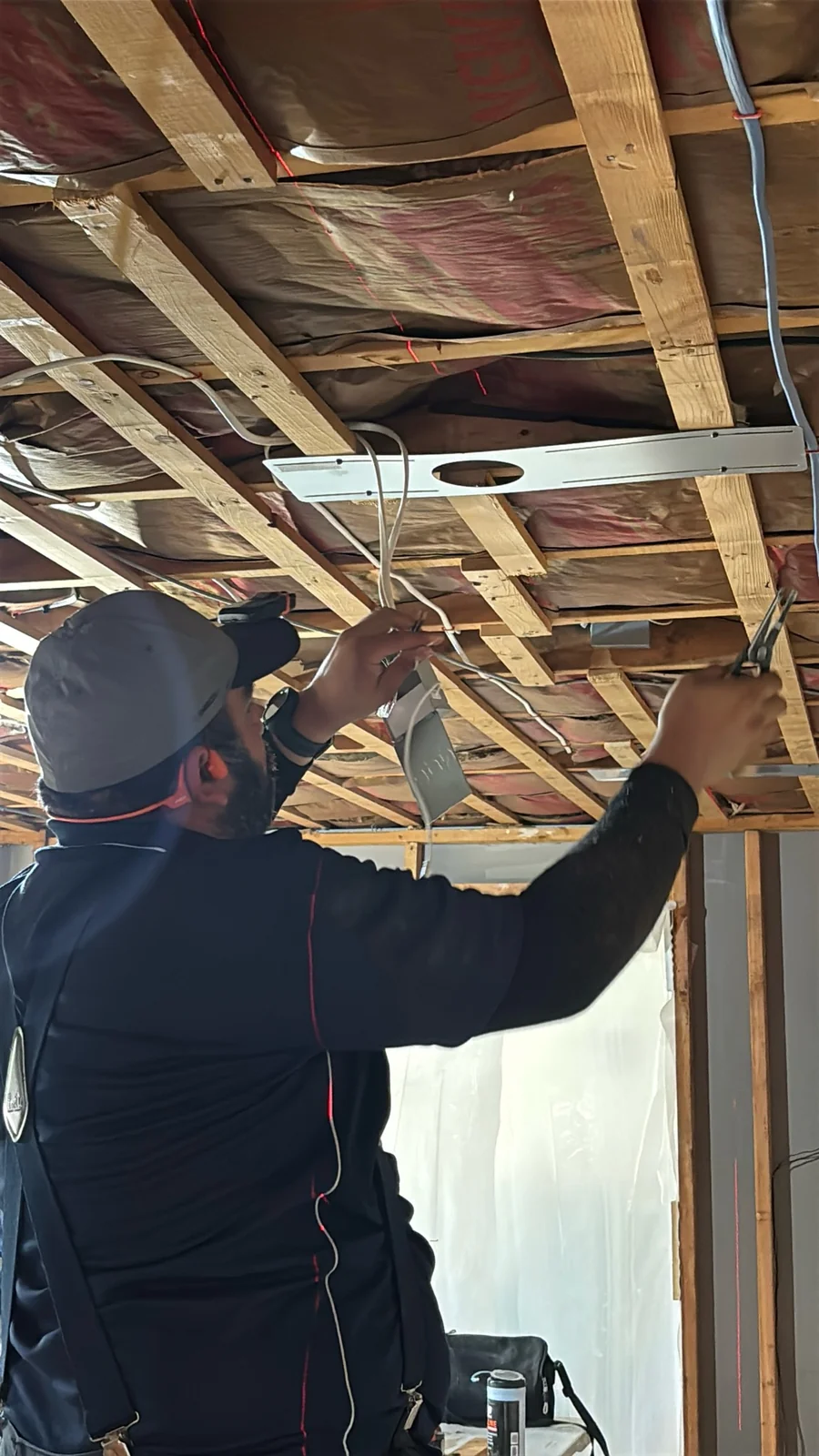 Sylvester electrician working on overhead wiring in exposed framing