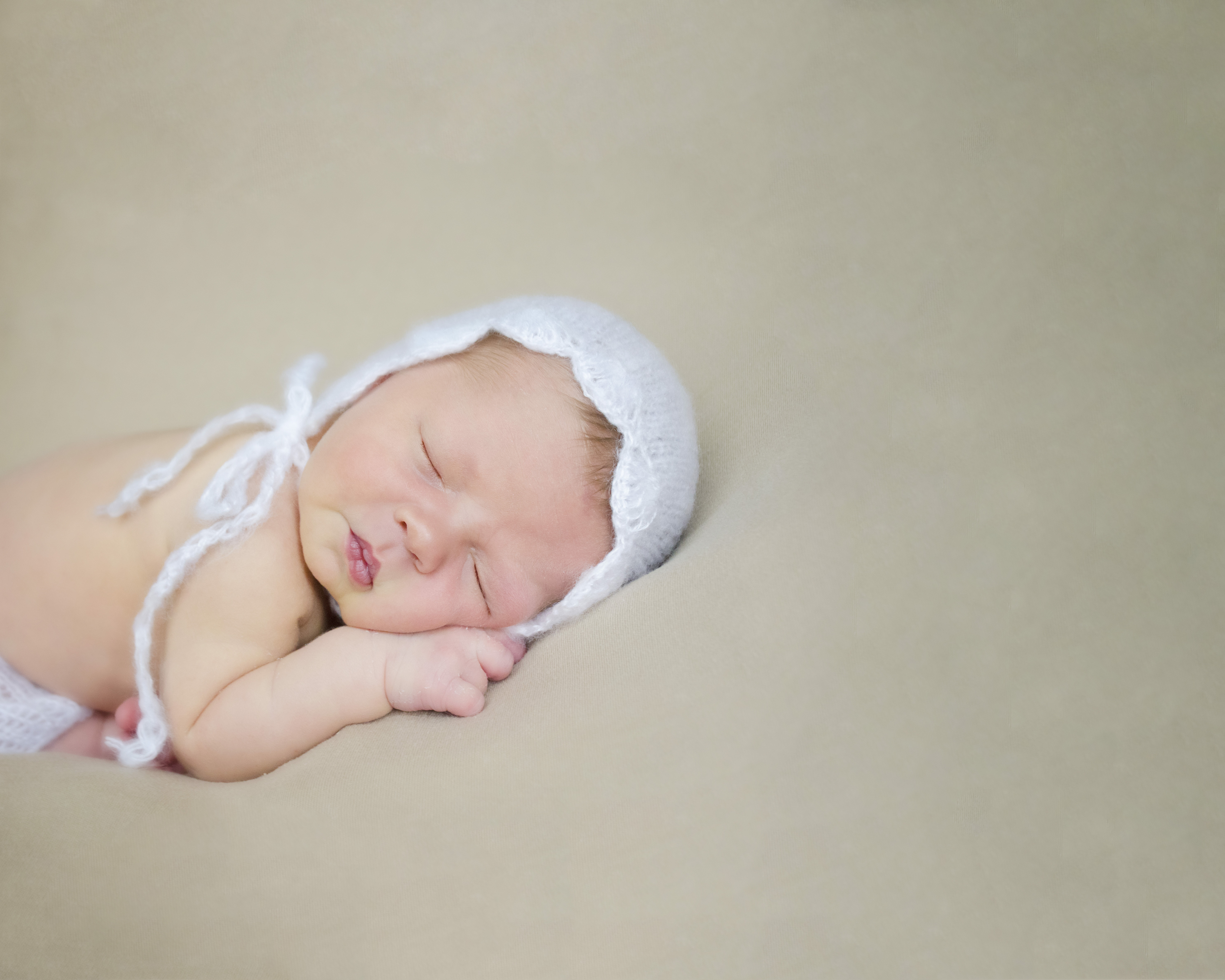 Newborn snuggled up on her belly with a bonnet on.