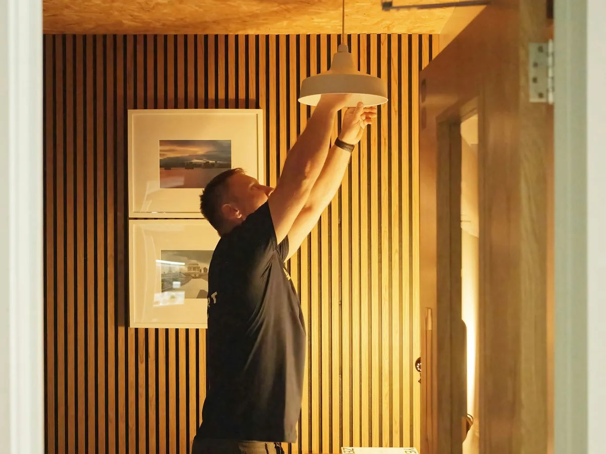 Electrician fitting a pendant light in a wood-panelled room
