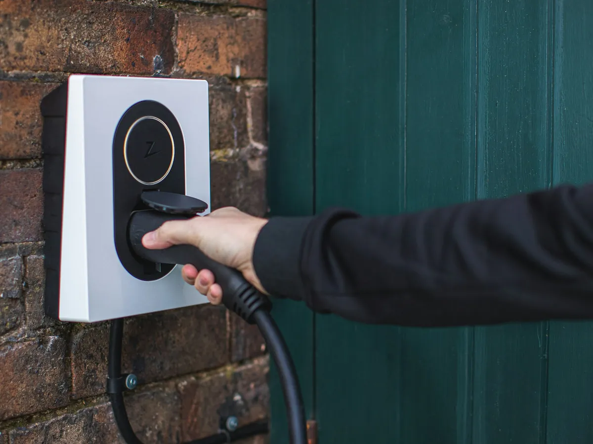 Home EV charger on a brick wall, cable being plugged in