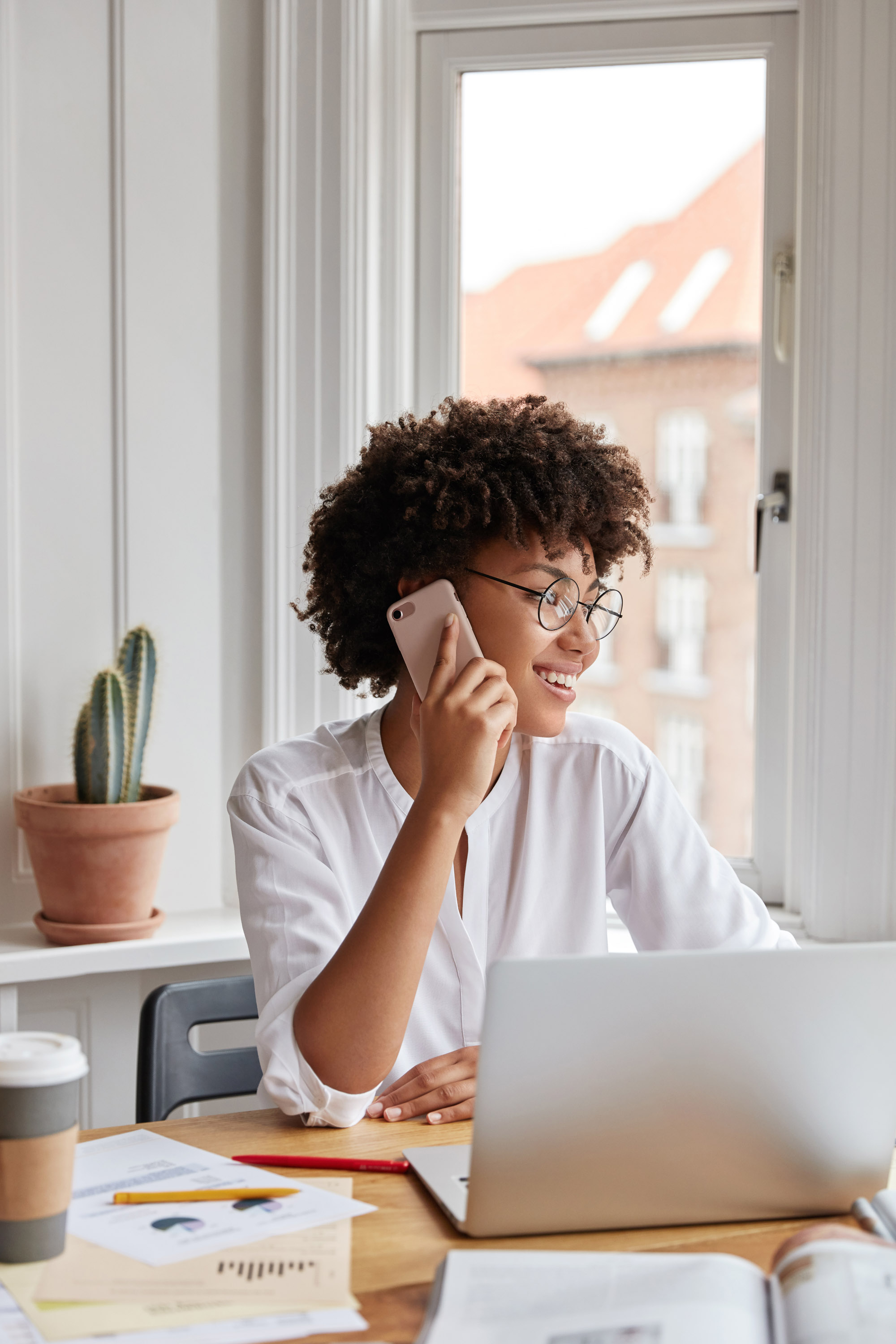 Young woman in a white blouse talking on a smartphone at a desk