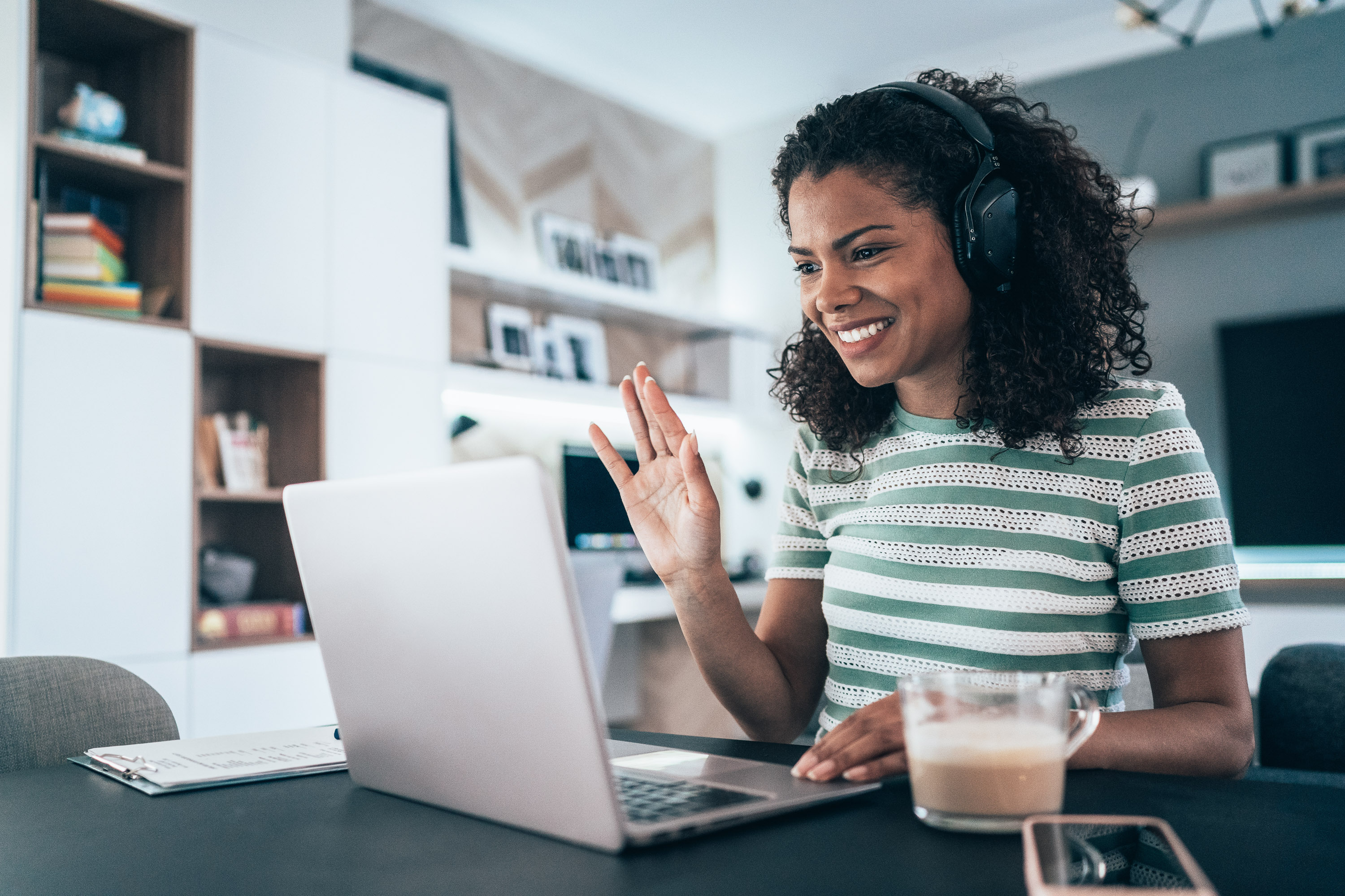 Woman in headphones waving at a laptop screen