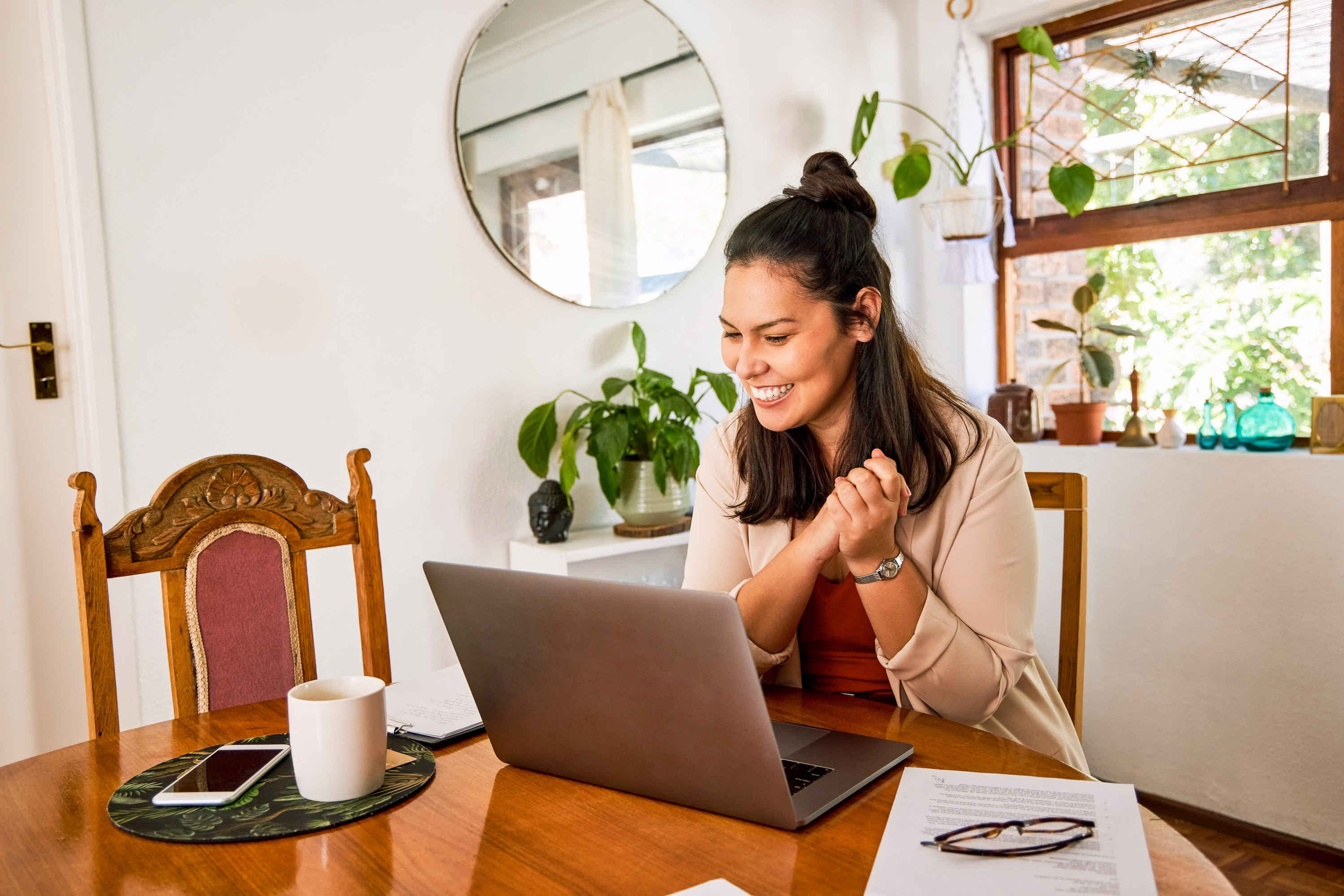 Woman in a cream blazer clasping her hands at a laptop