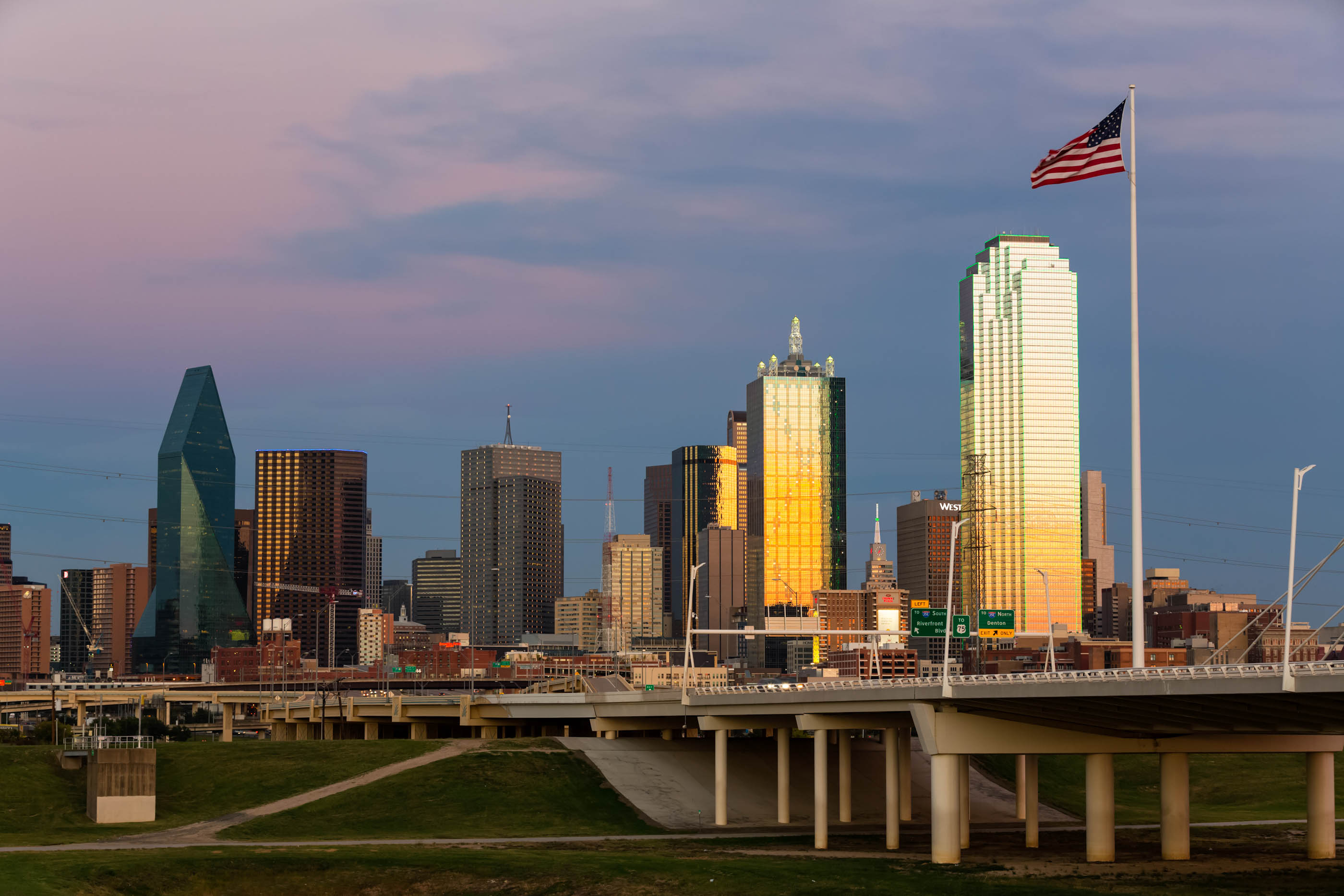 Dallas skyline from the Trinity levee with a US flag at golden dusk