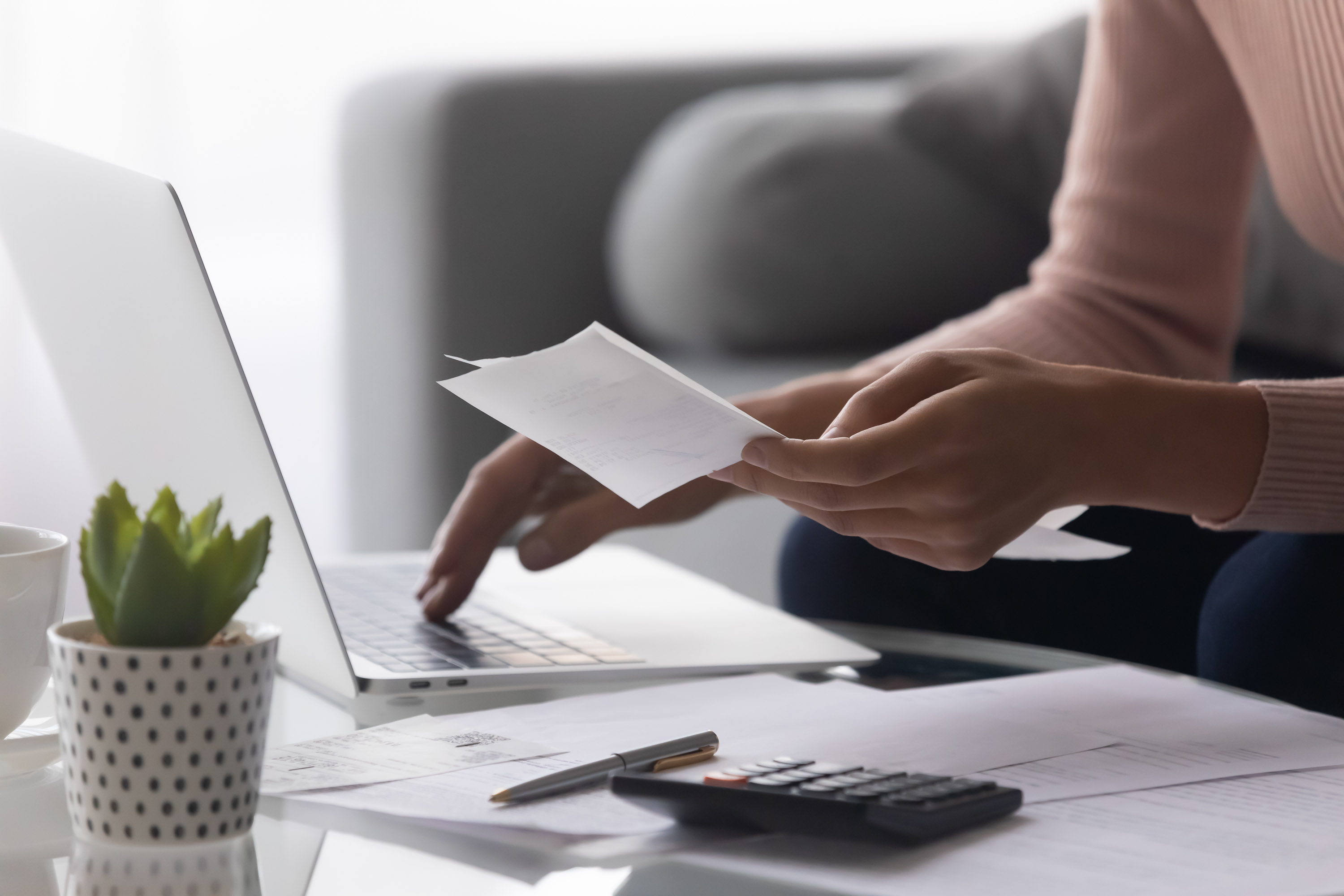 Woman's hands holding a receipt while typing on a laptop