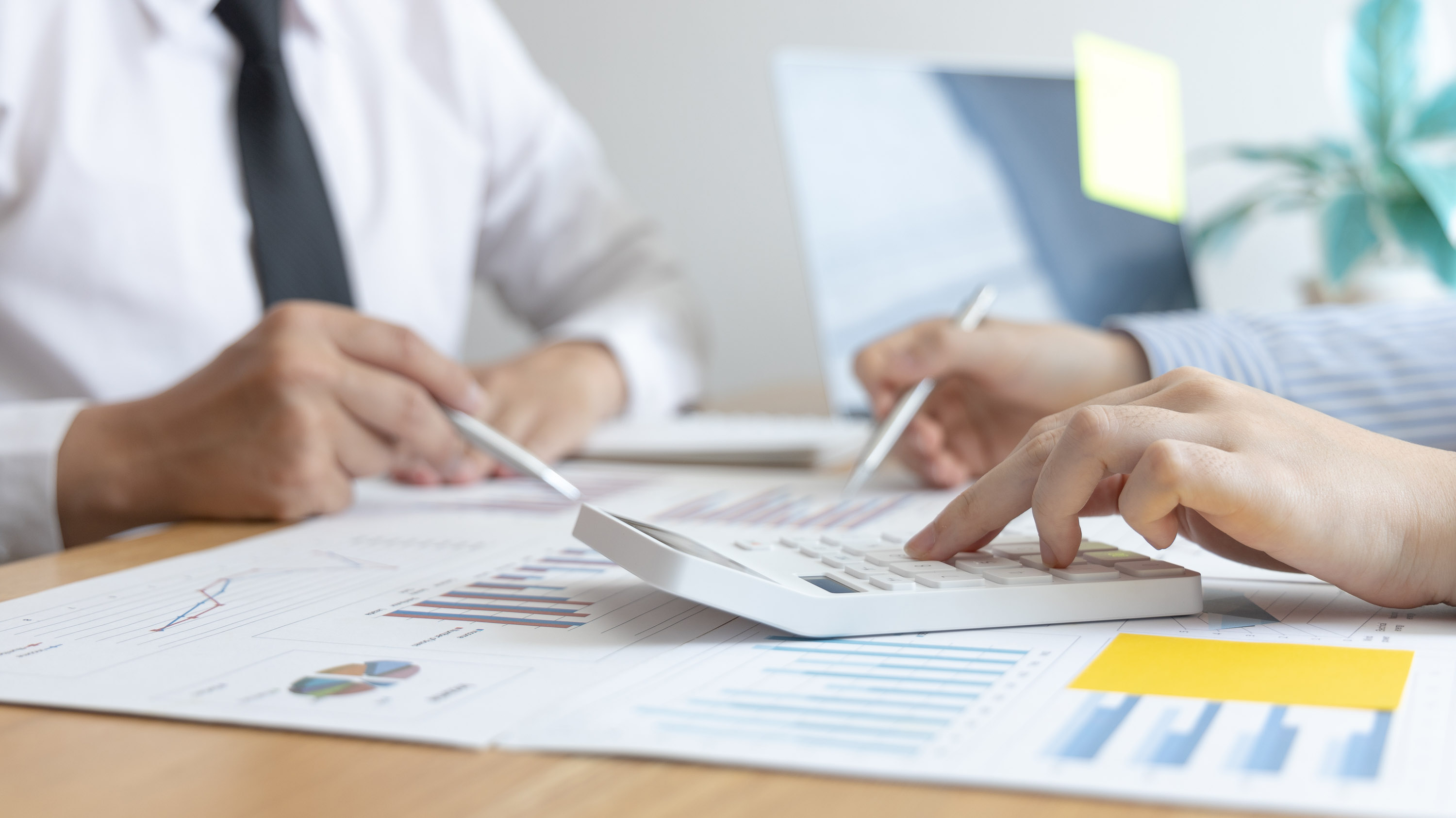 Two pairs of hands using a calculator over printed charts