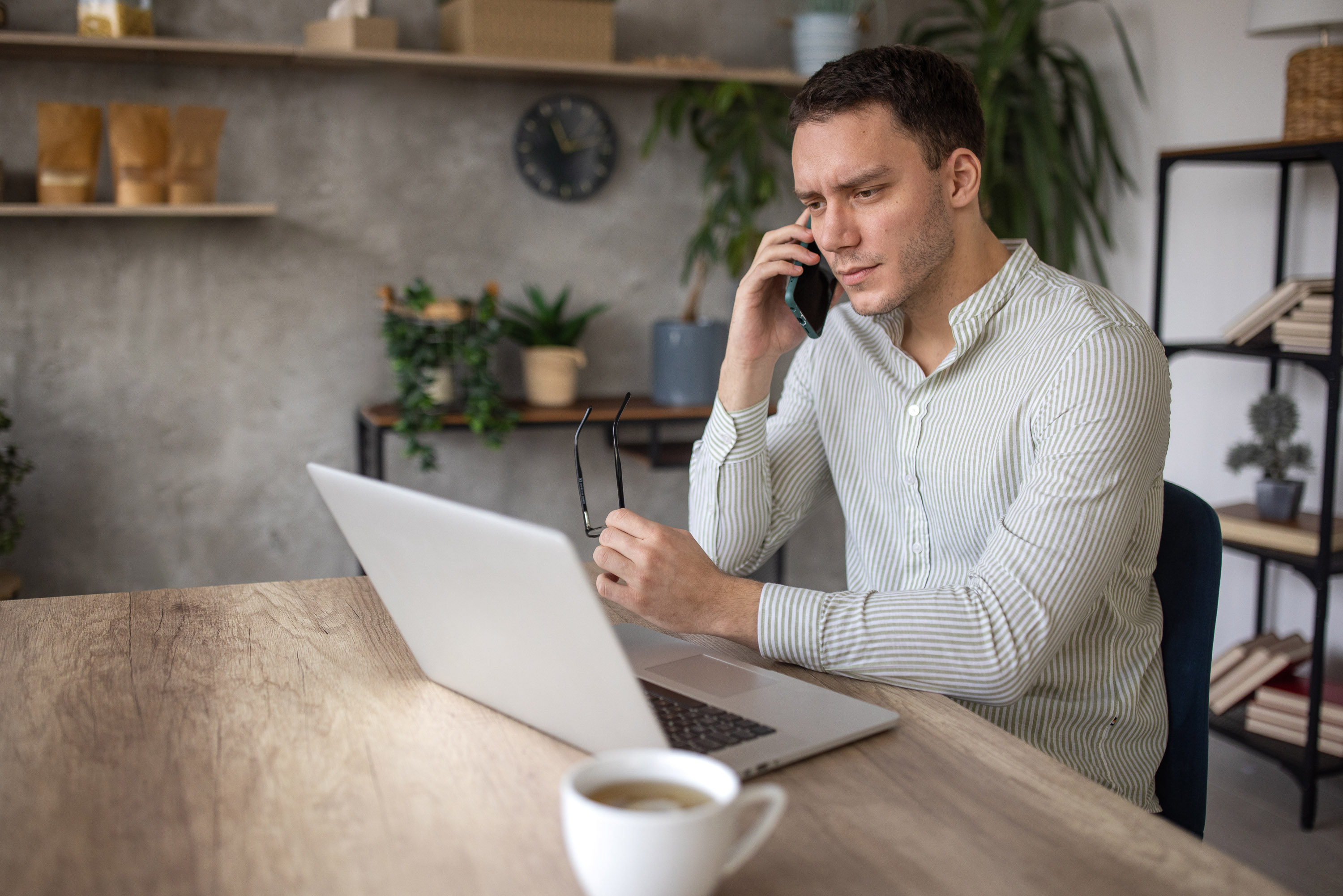 Man in a striped shirt on a phone call while reading a laptop screen