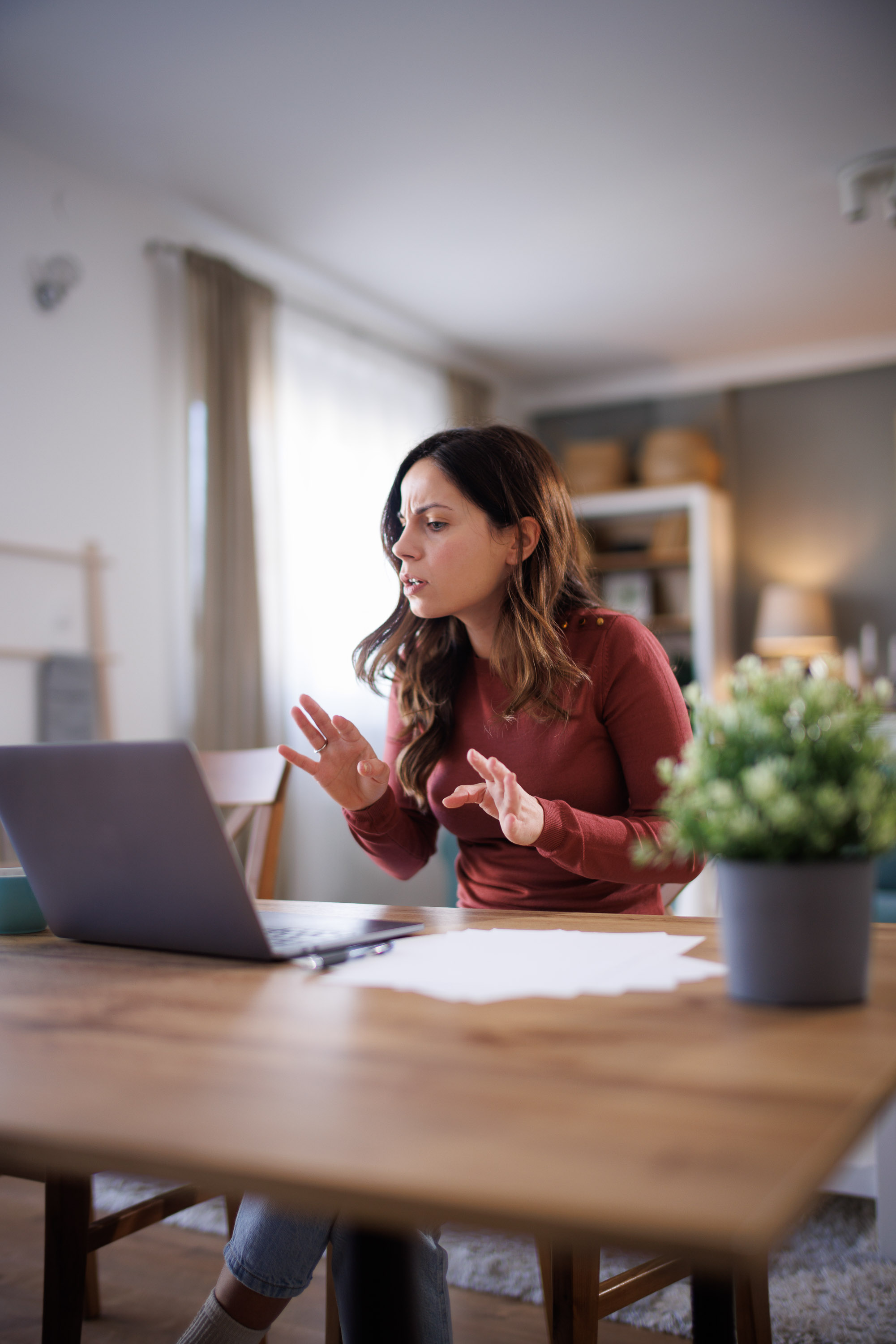 Woman in rust top gesturing while speaking at a laptop