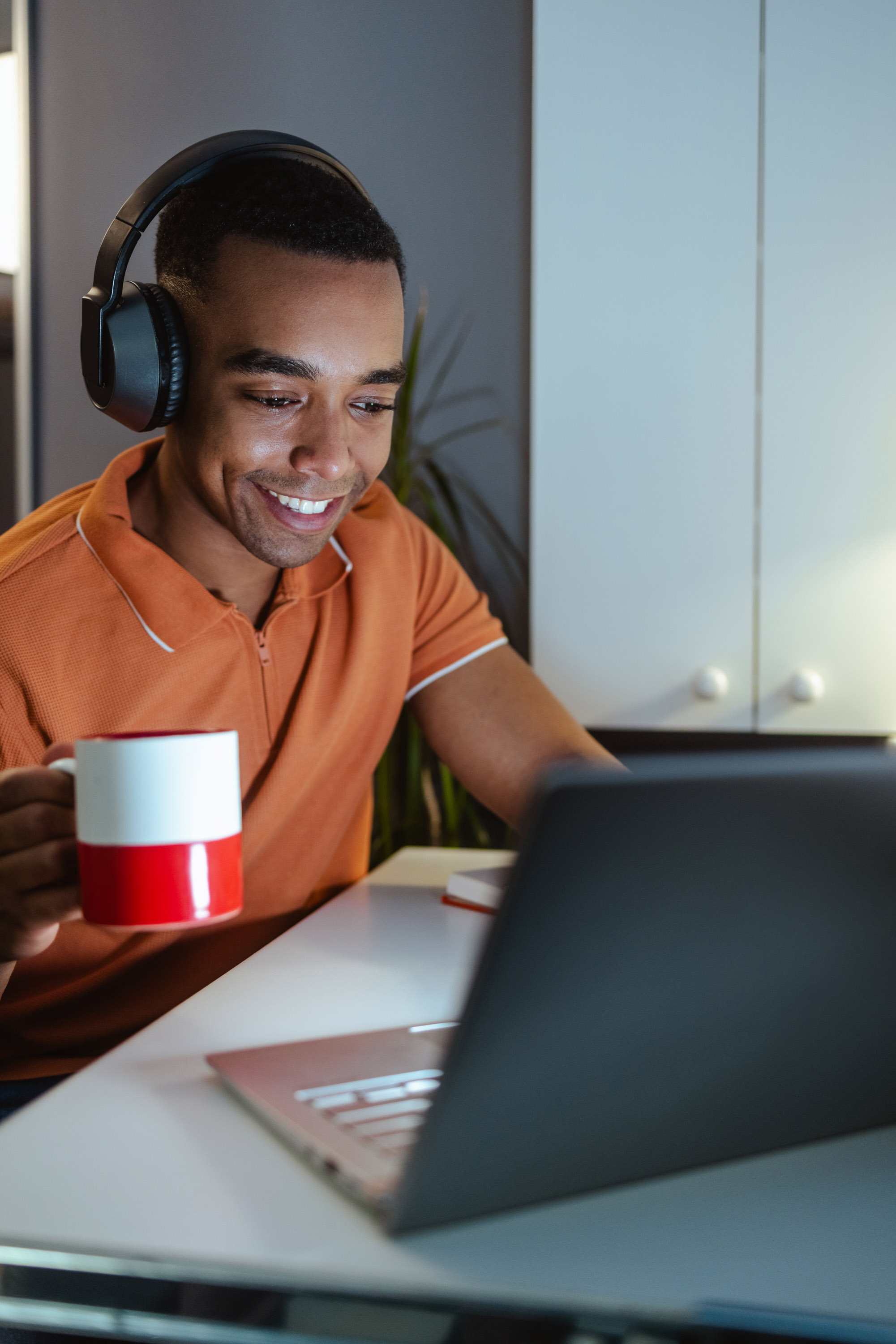 Young man in orange polo with headphones smiling at a laptop
