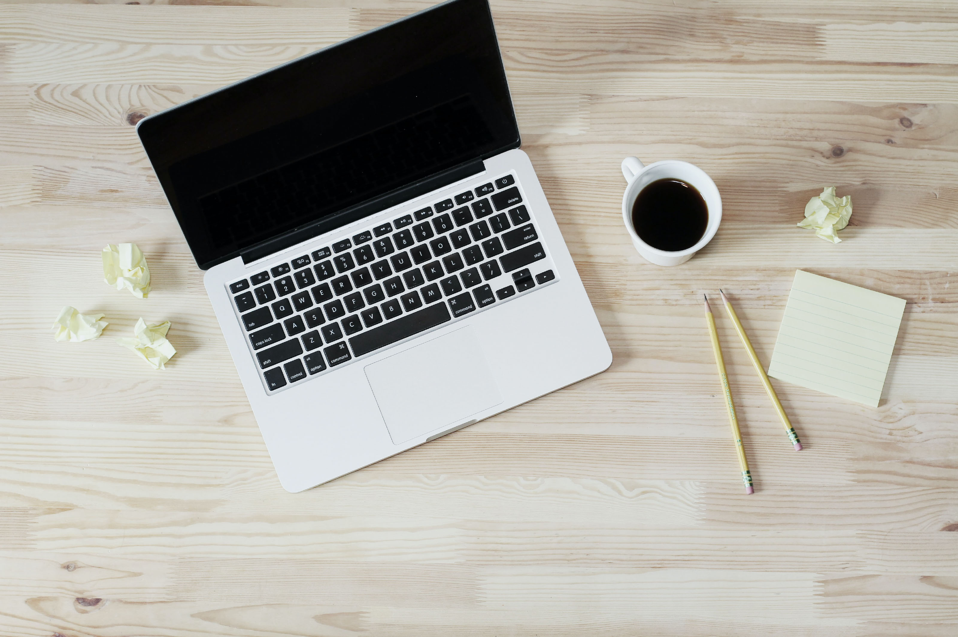 Open laptop on a wooden desk with a coffee cup and pencils