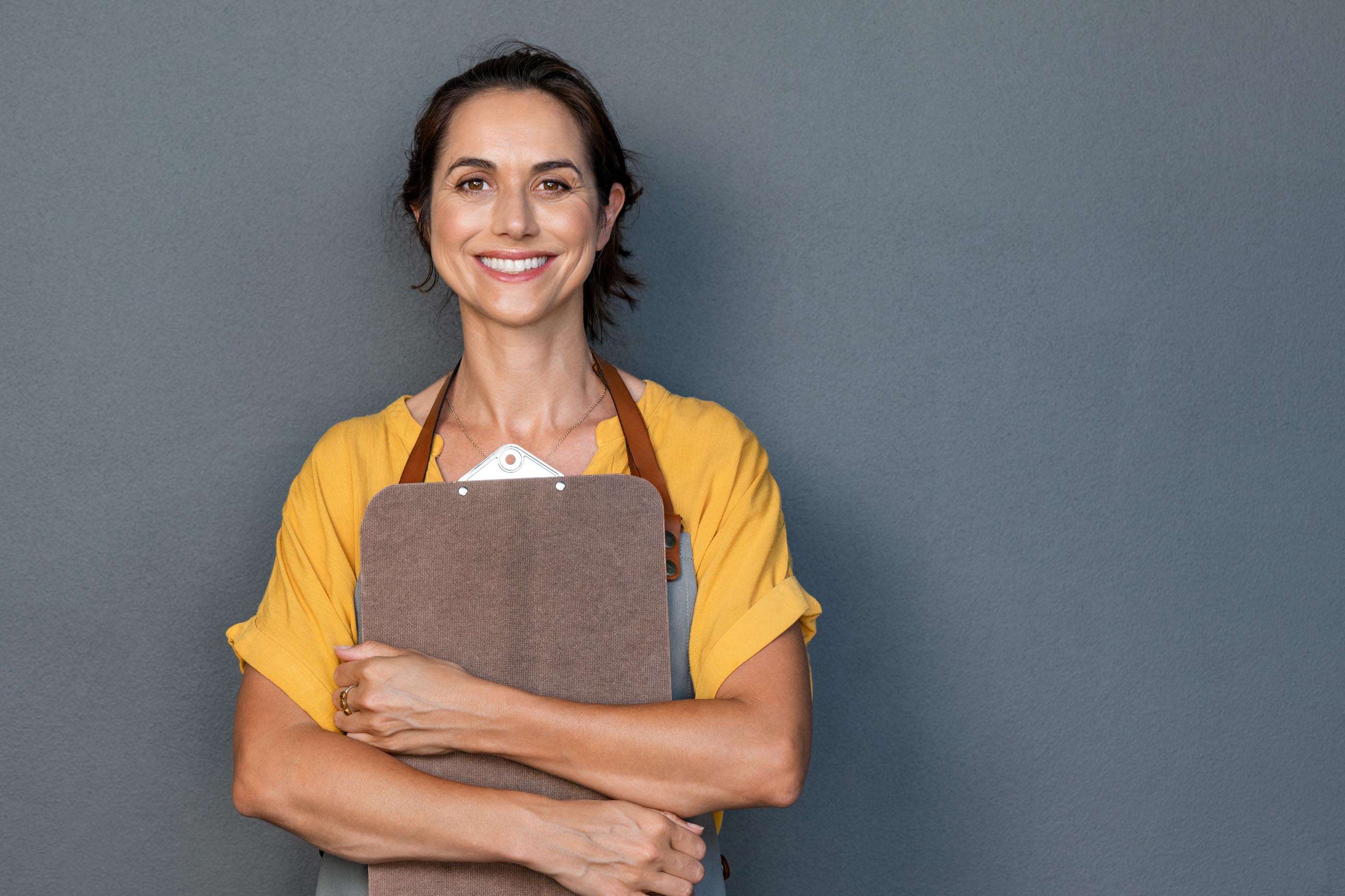 Smiling woman in a leather apron hugging a clipboard