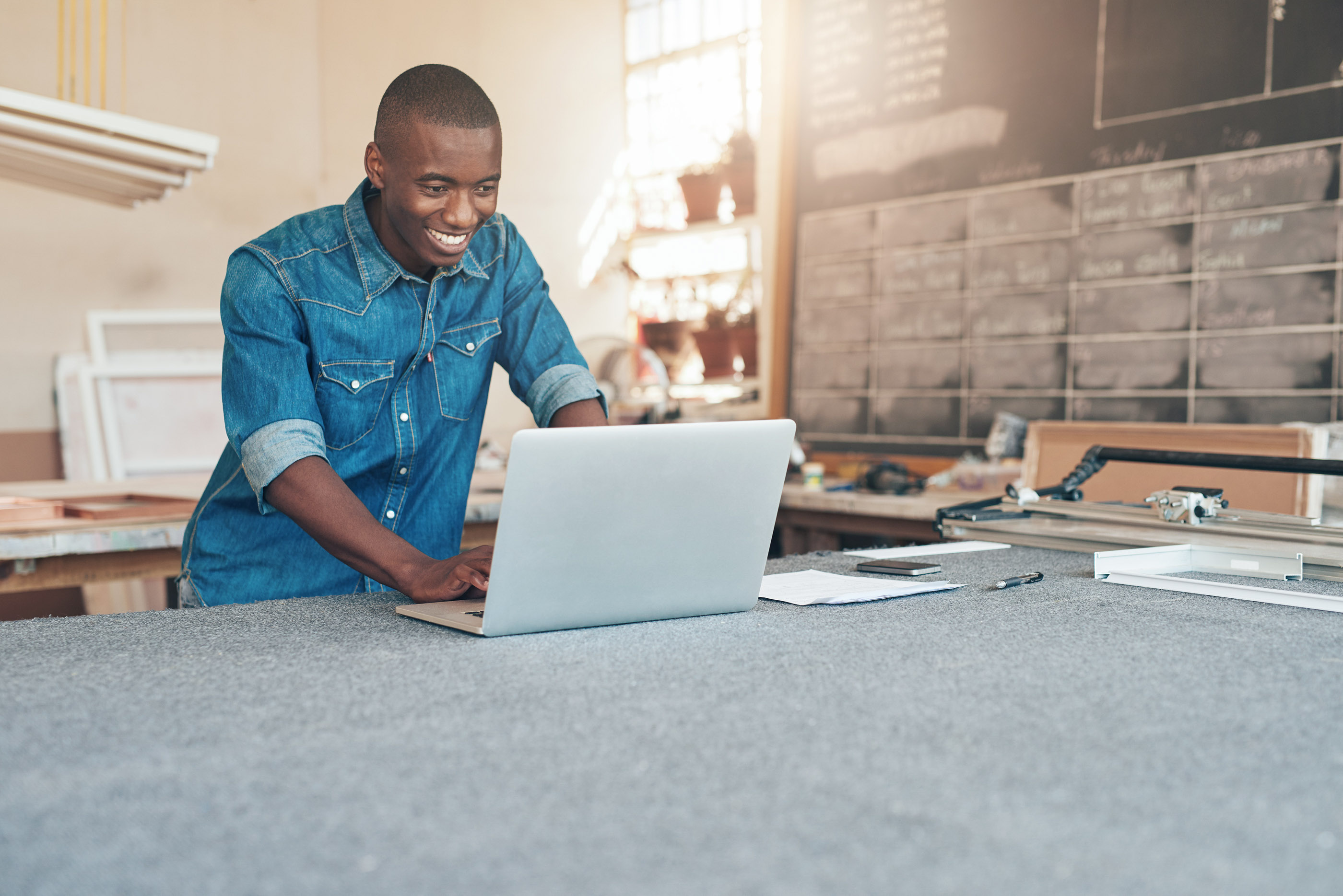 Young man in a denim shirt using a laptop at a workshop counter