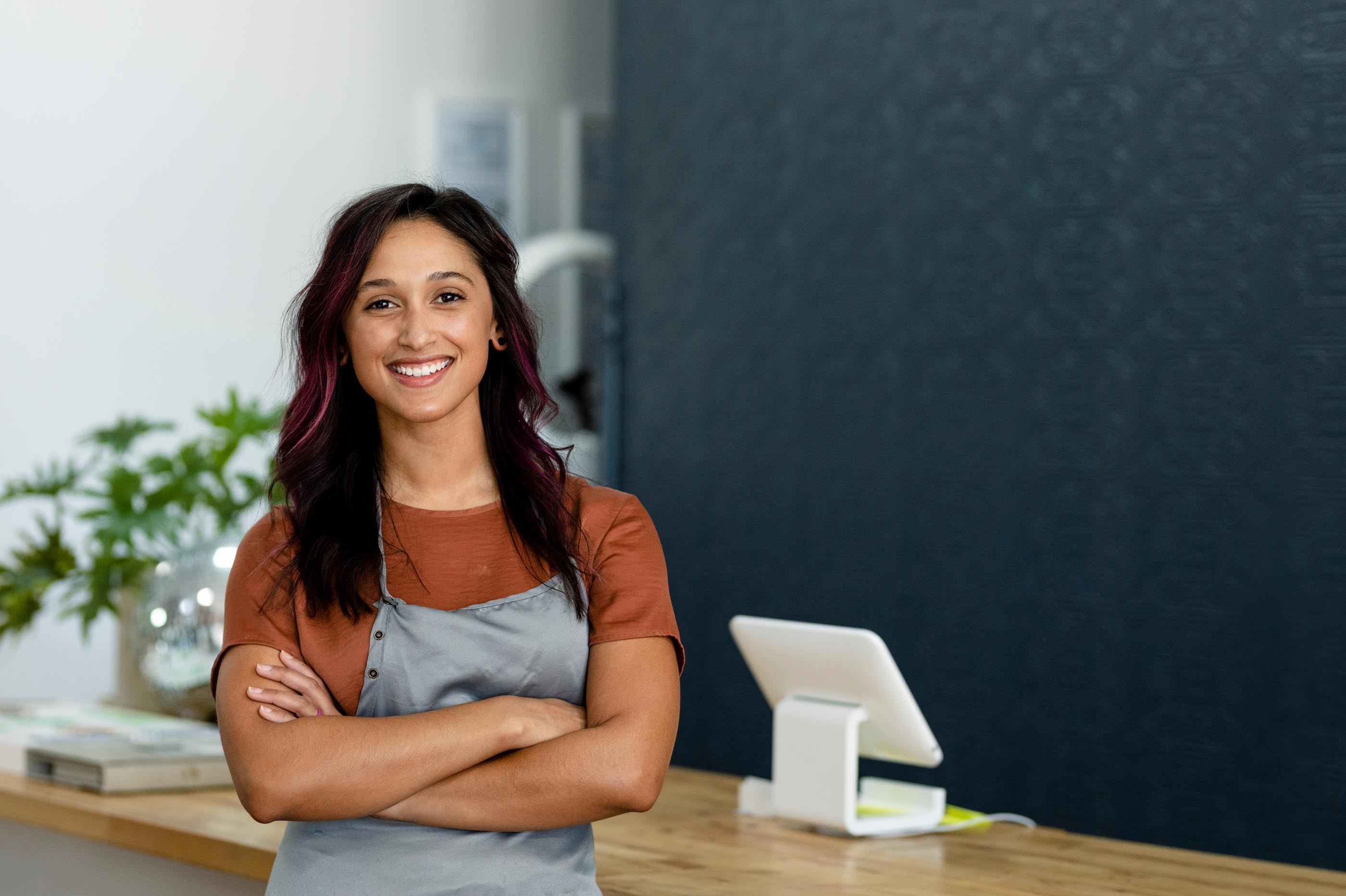 Smiling shop worker in gray apron by a tablet point-of-sale