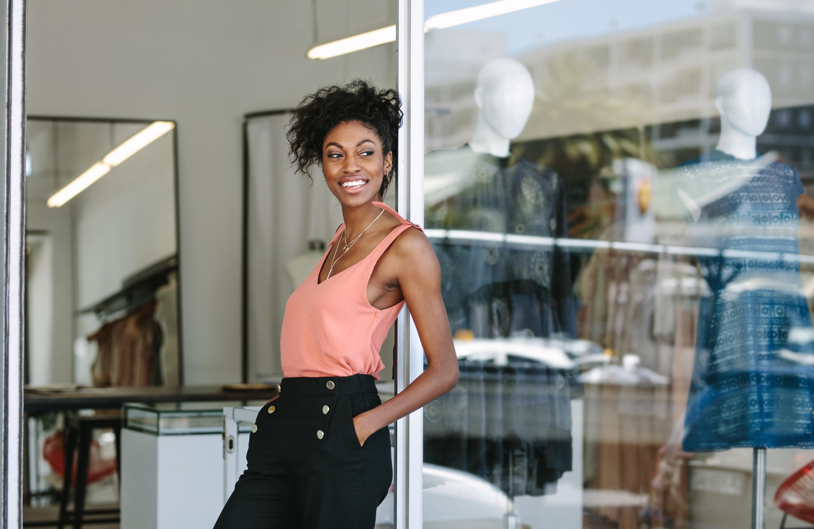Young woman leaning in a boutique doorway with hands in pockets