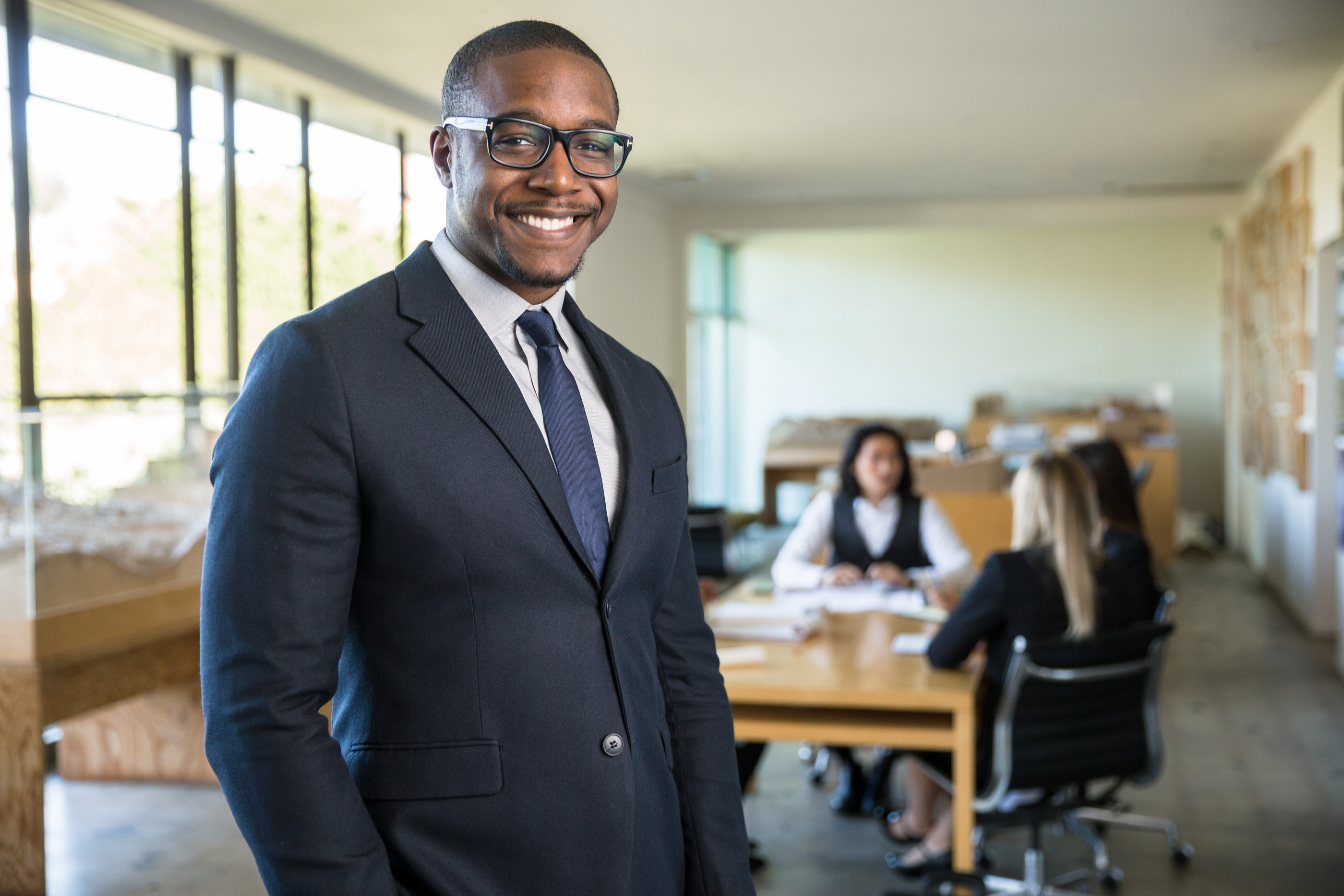 Man in a charcoal suit and glasses standing in an open office