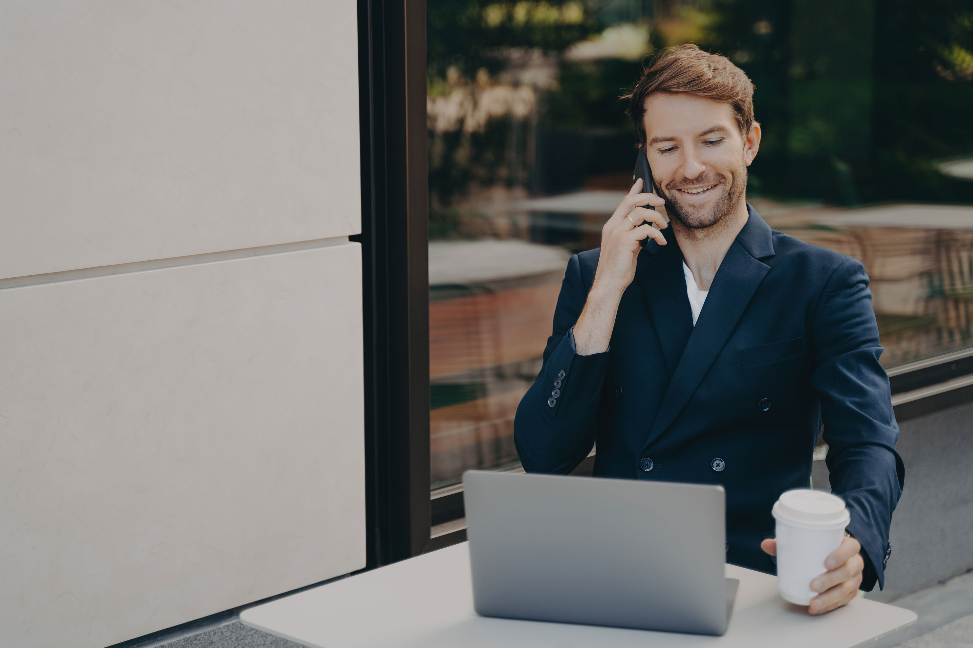 Bearded man in a navy blazer on a phone call beside a laptop