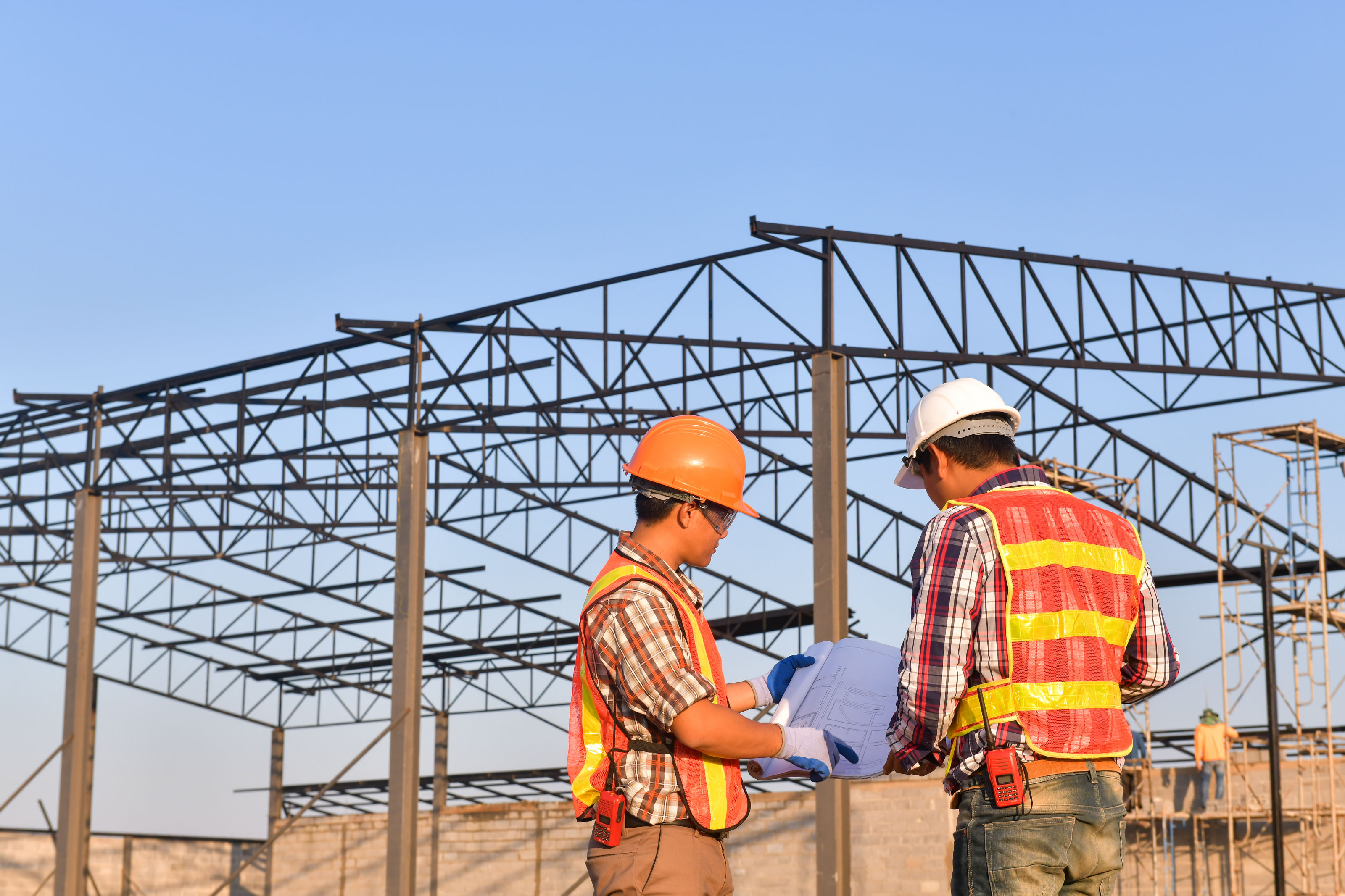 Two construction workers reviewing a blue drawing on a steel-frame site