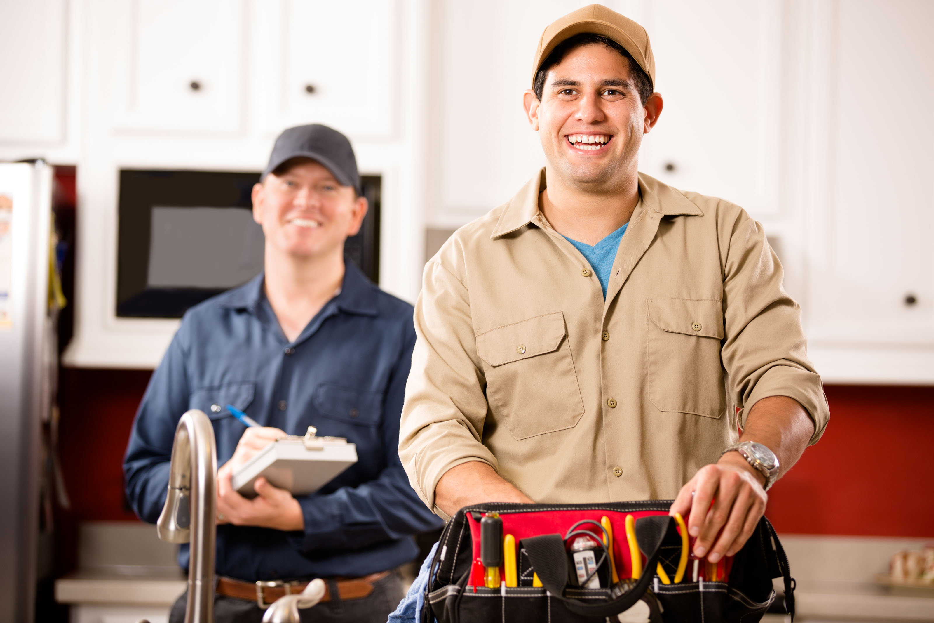 Smiling man in tan work shirt leaning on an open tool bag
