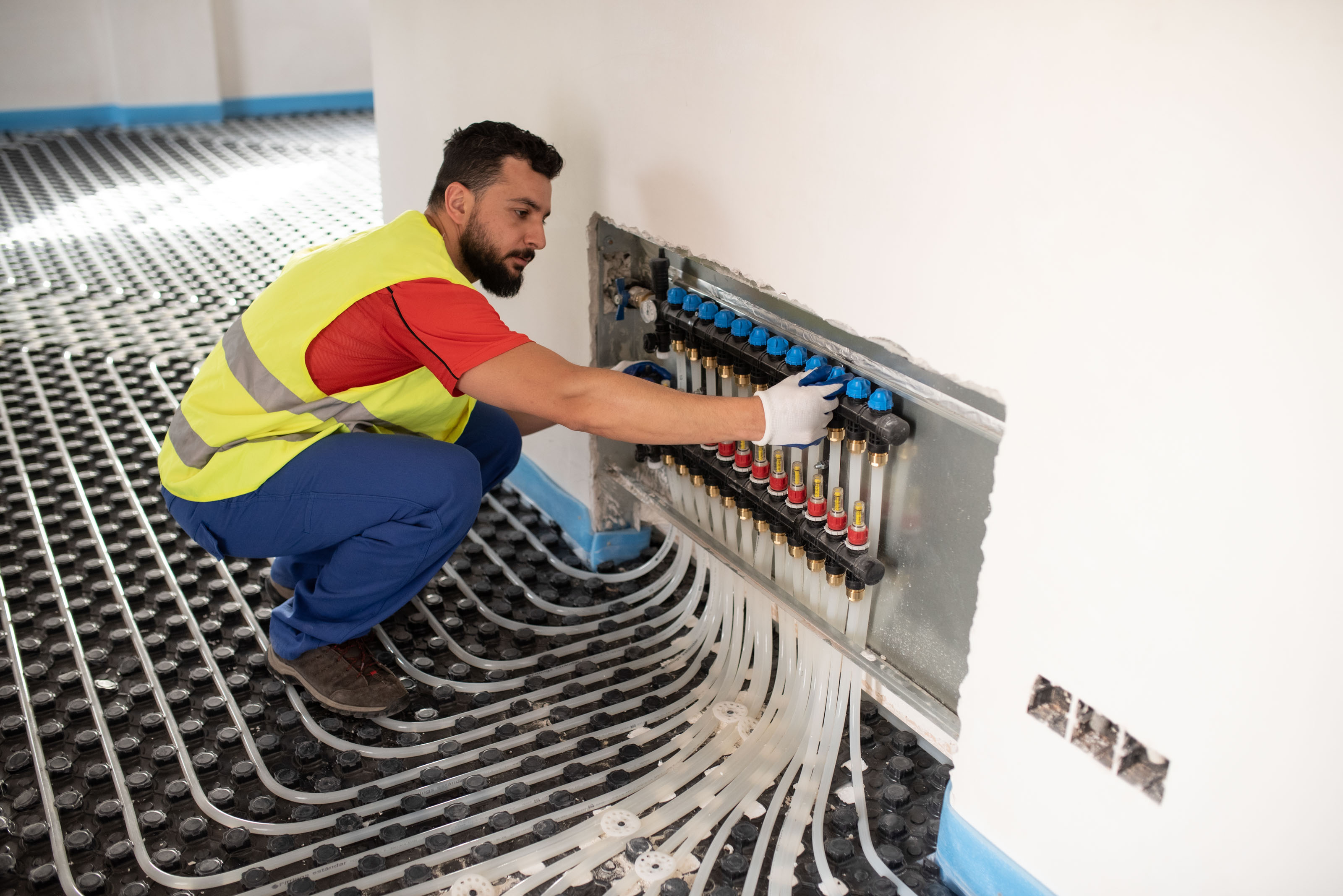 Crouching heating engineer adjusting an underfloor heating manifold