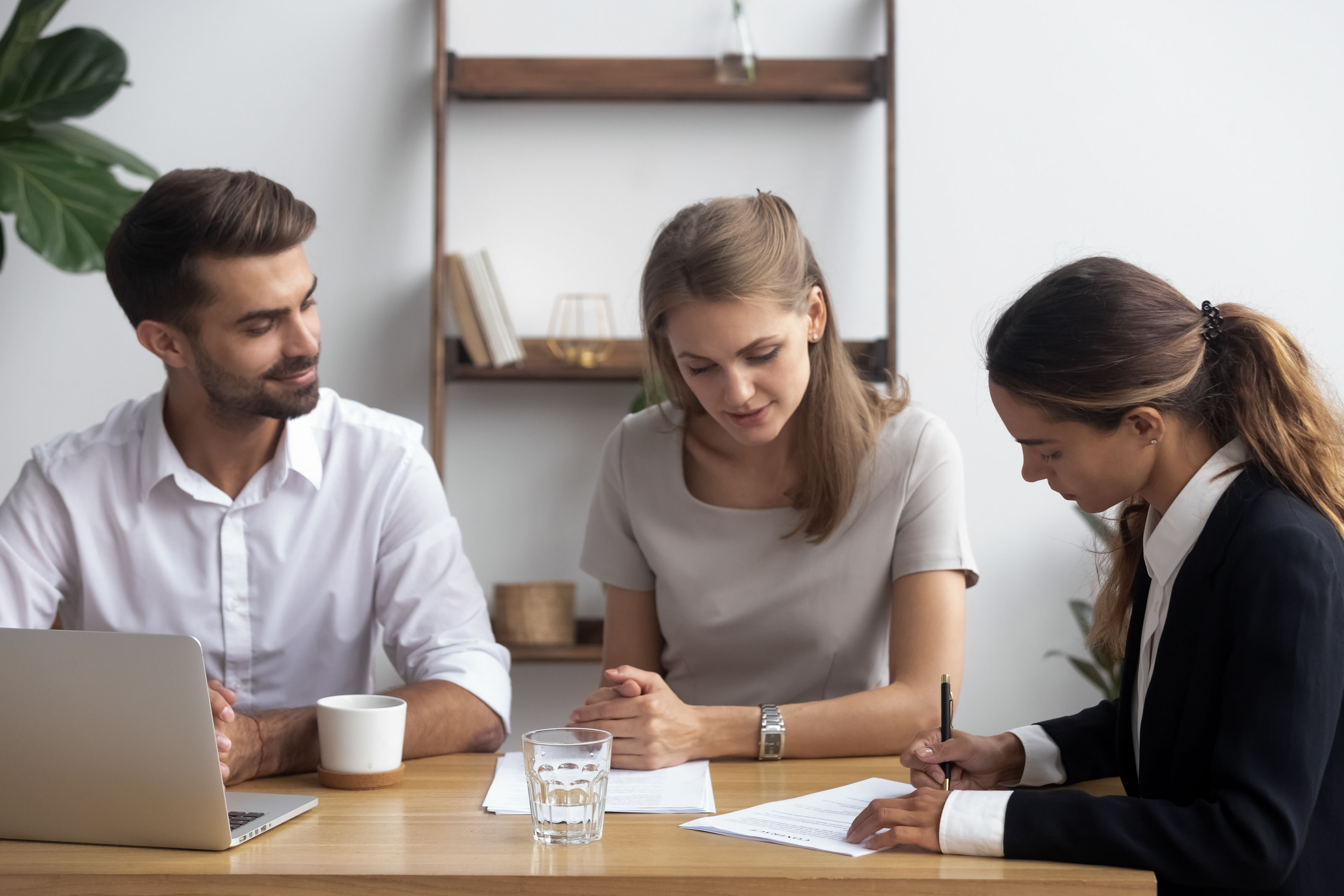 Woman in black blazer signing a contract beside a seated couple