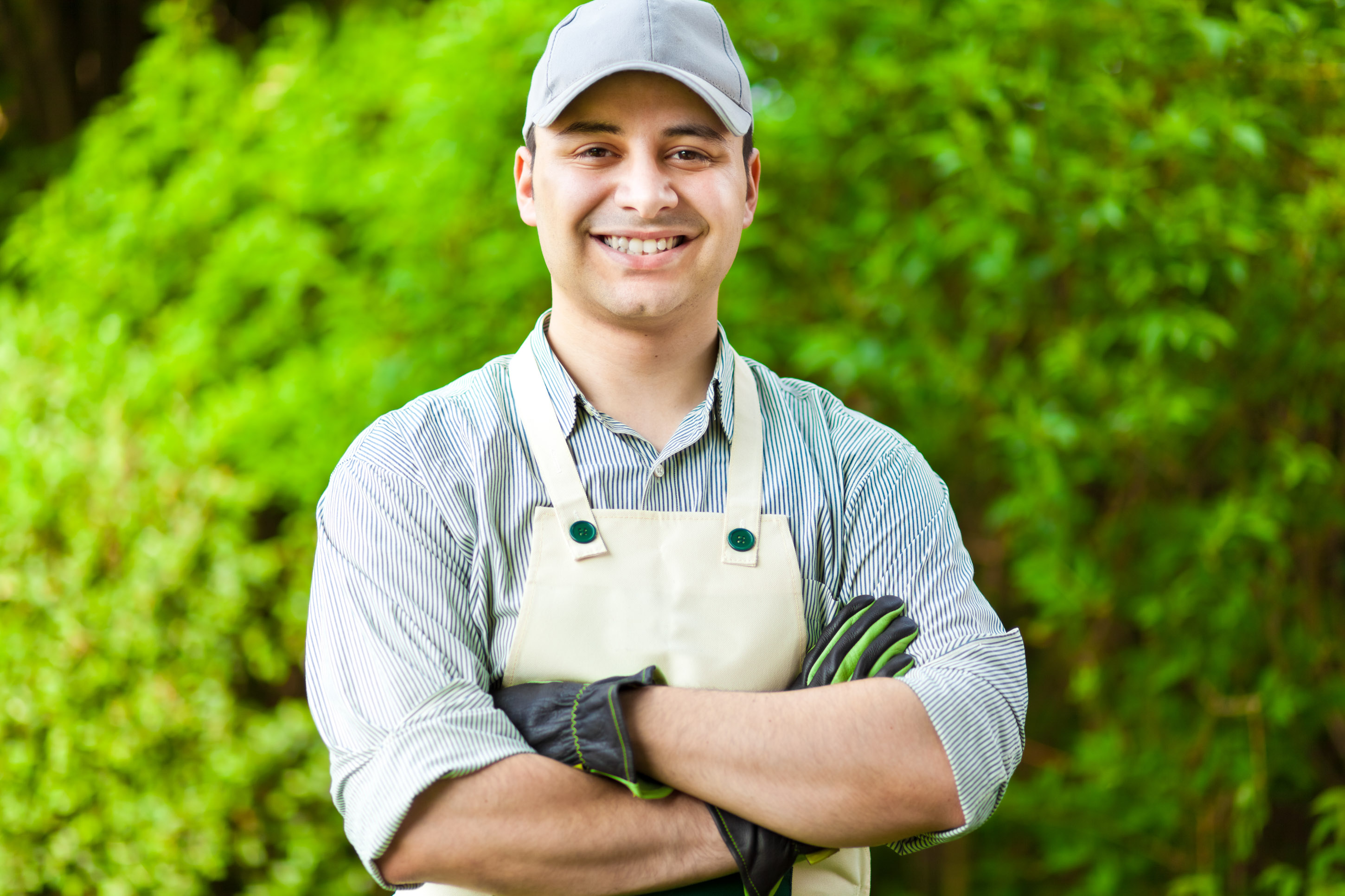 Smiling young gardener in a cream apron with arms crossed