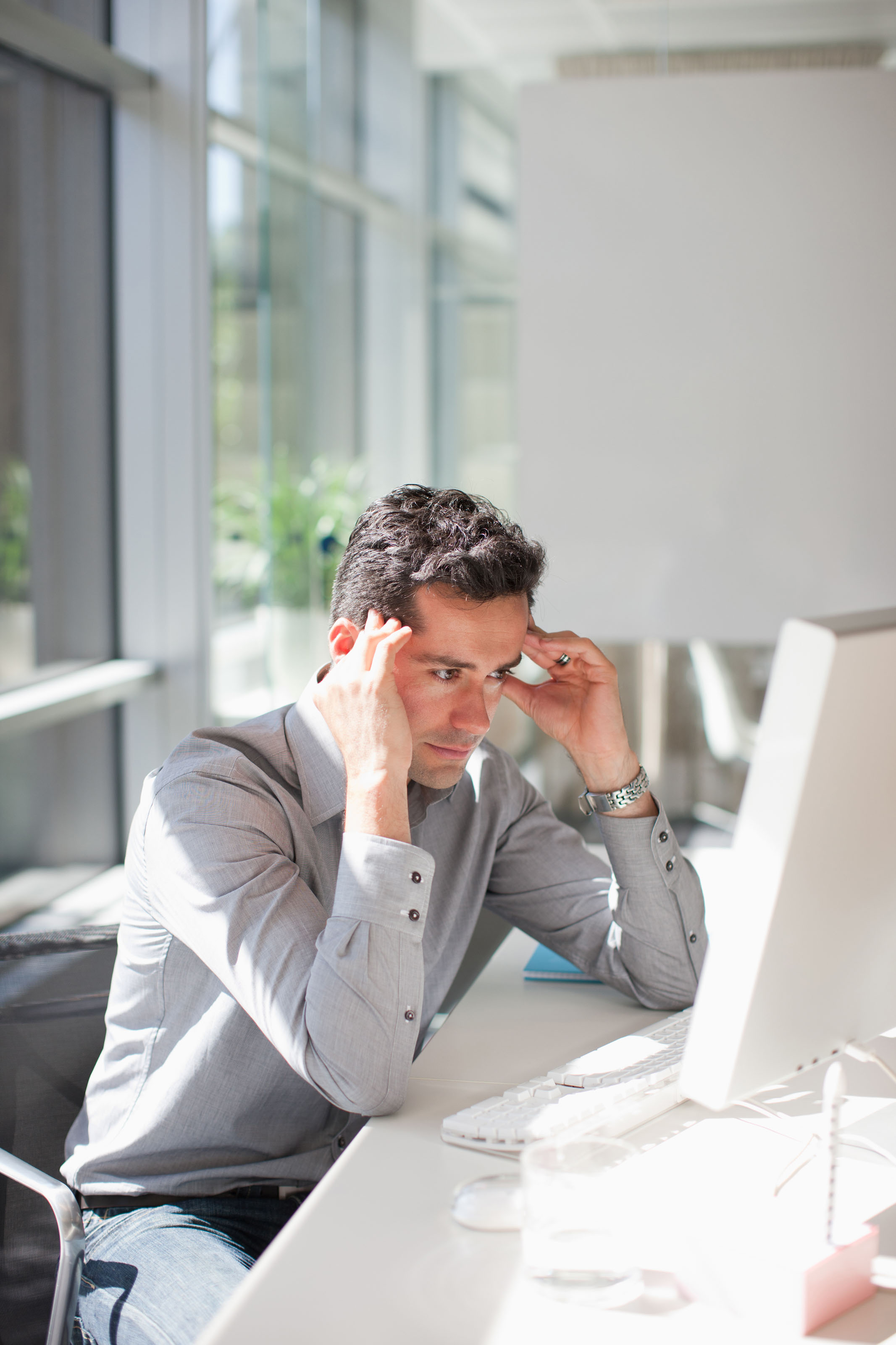 Man in gray henley rubbing his temples at a desk