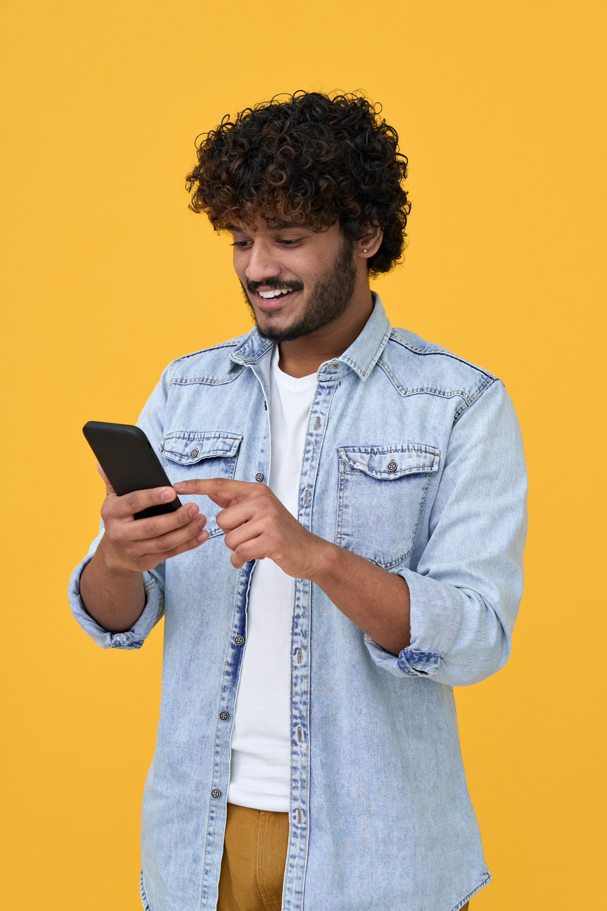 Smiling young man in a denim shirt tapping a smartphone