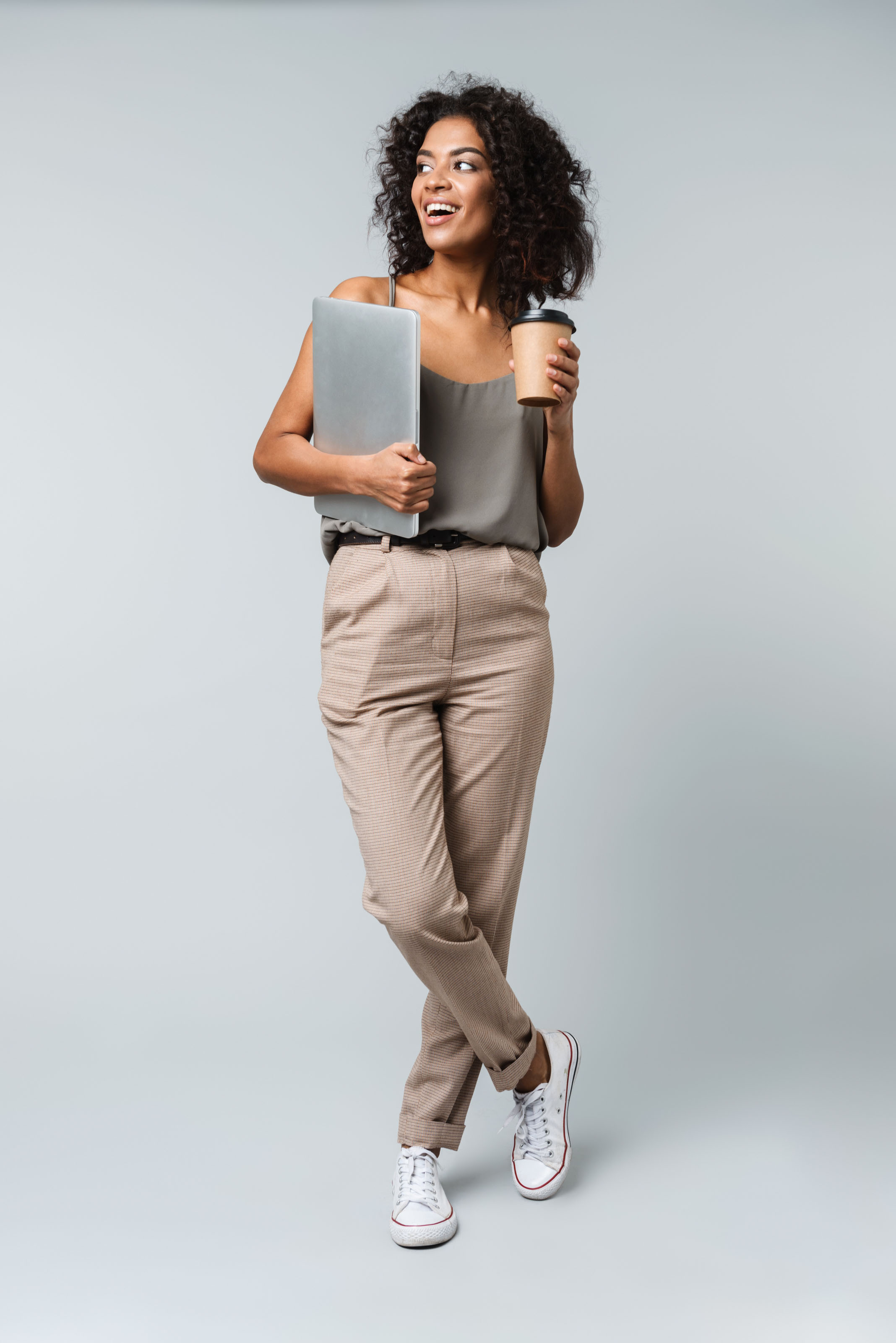 Young woman walking with a laptop under her arm and a coffee cup
