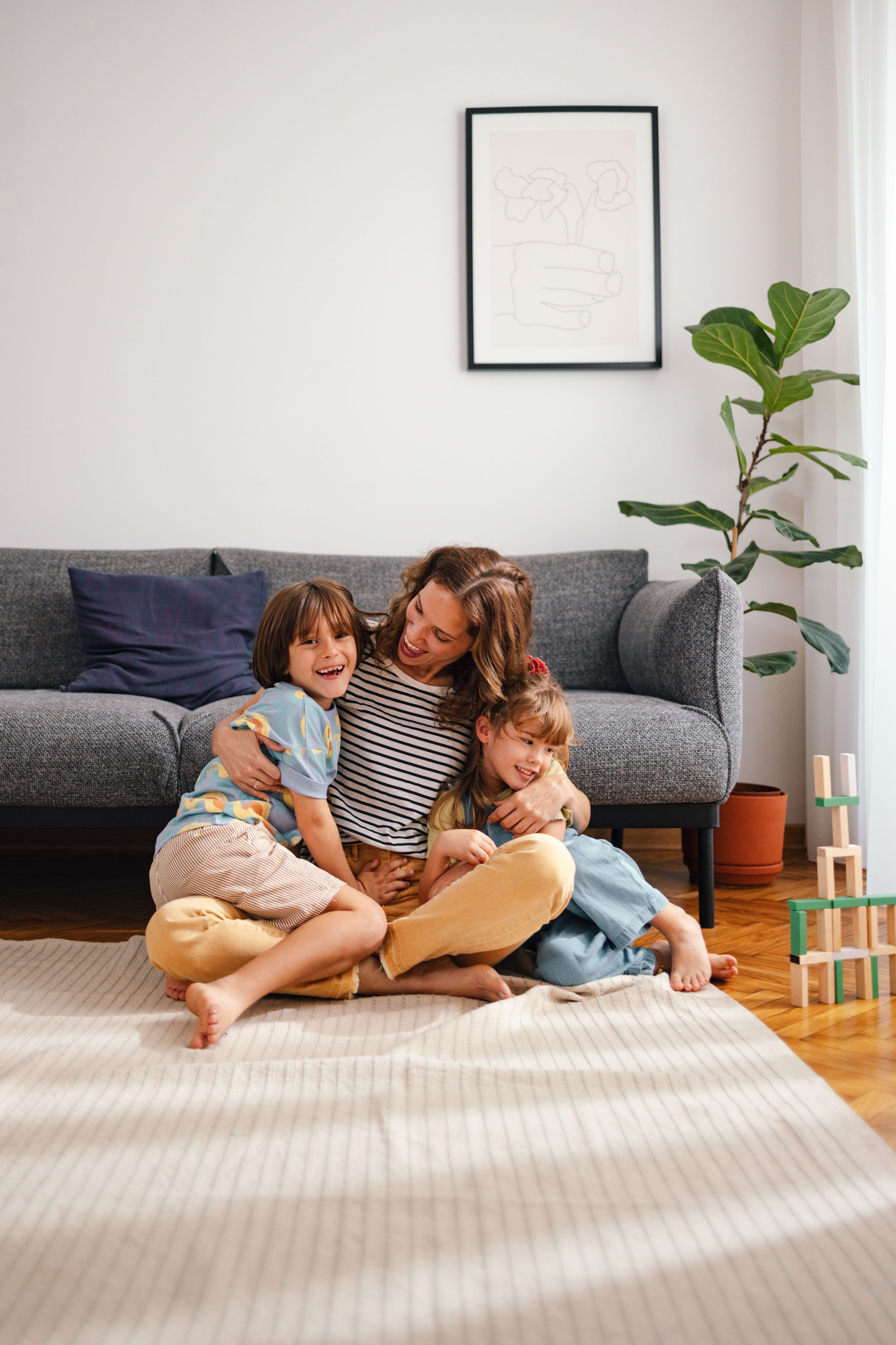 Laughing woman hugged by two young children on a living-room floor