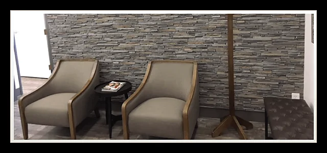 Waiting area with grey armchairs beside the stone feature wall at Southland Denture Clinic