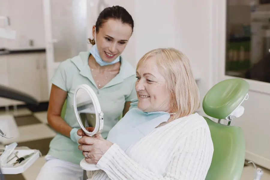 Senior patient looking into a hand mirror beside a dental professional (stock photo)
