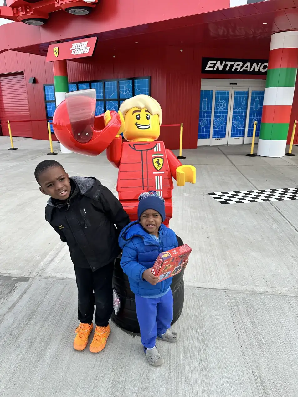 Two Black brothers standing in front of the LEGO Ferrari Build and Race entrance at LEGOLAND New York holding a LEGO set
