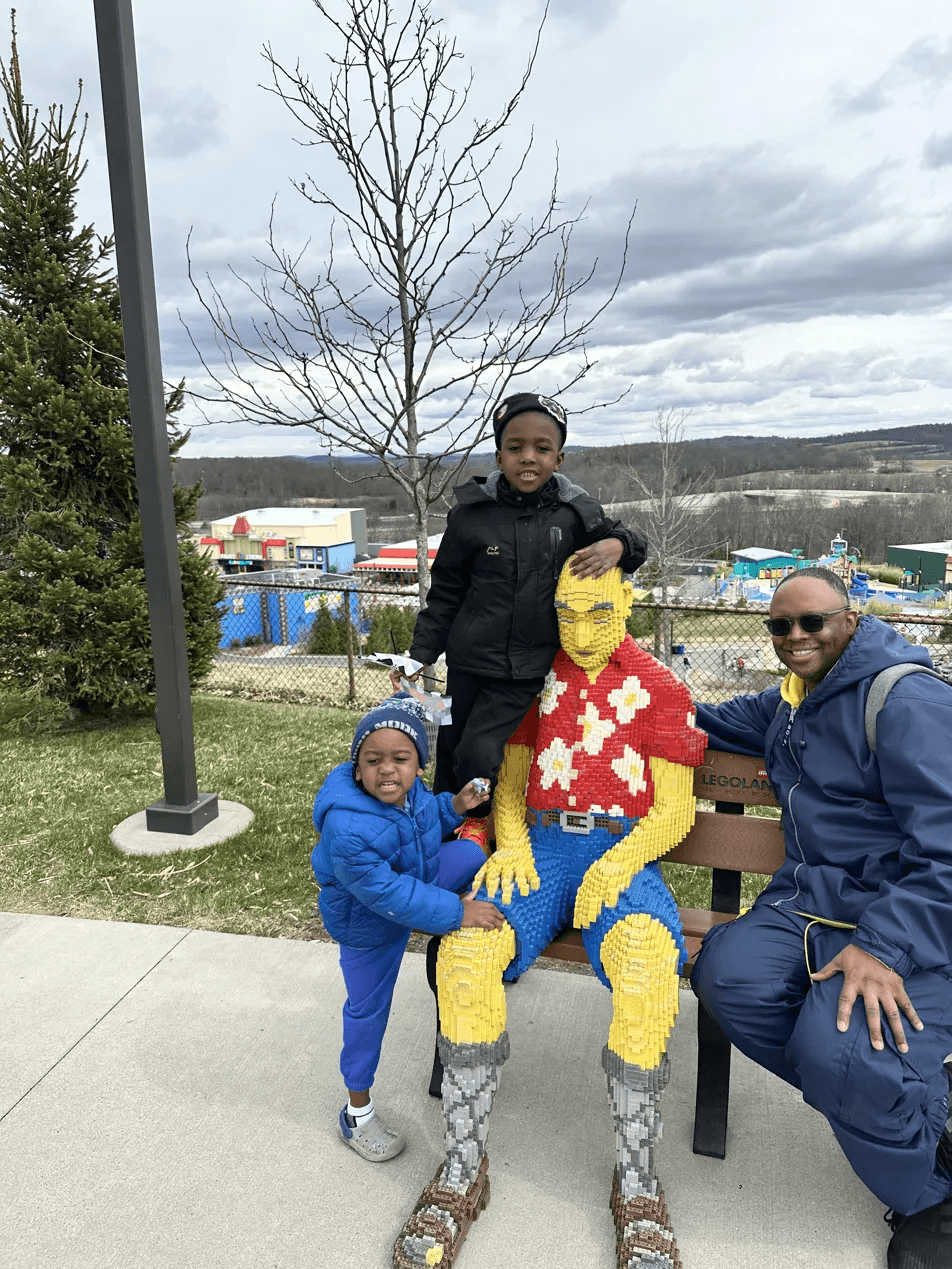 Black family of two boys and dad sitting with LEGO sculpture overlooking LEGOLAND New York park and Hudson Valley