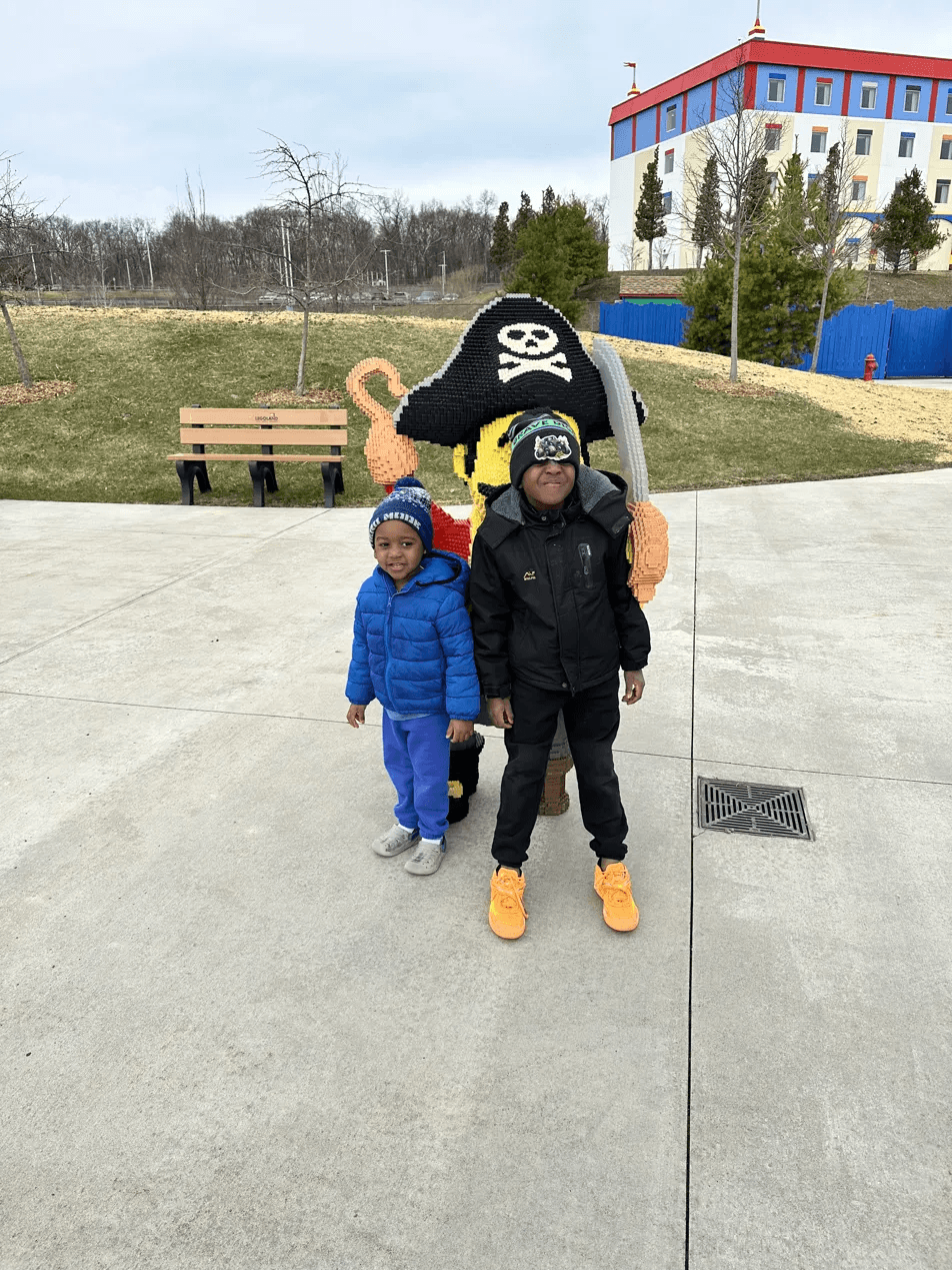 Black brothers posing with a giant LEGO pirate statue at LEGOLAND New York with the LEGO Hotel in the background