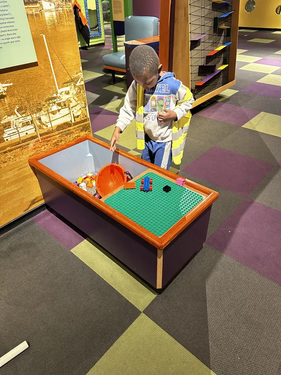 Young Black boy building with blocks at a hands-on activity table inside Maryland Science Center Kids Room