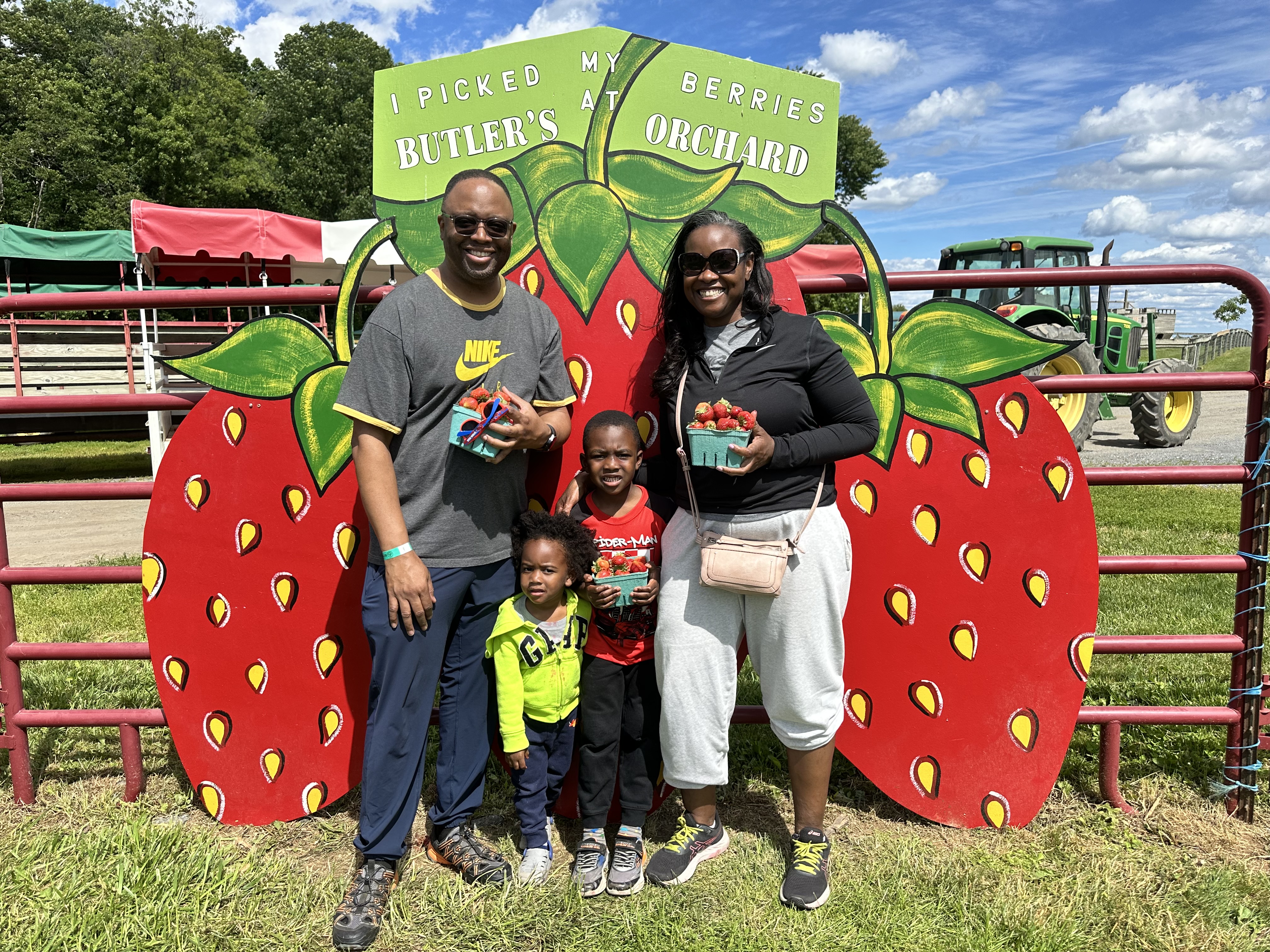Family of four standing together holding full strawberry baskets at Butler's Orchard