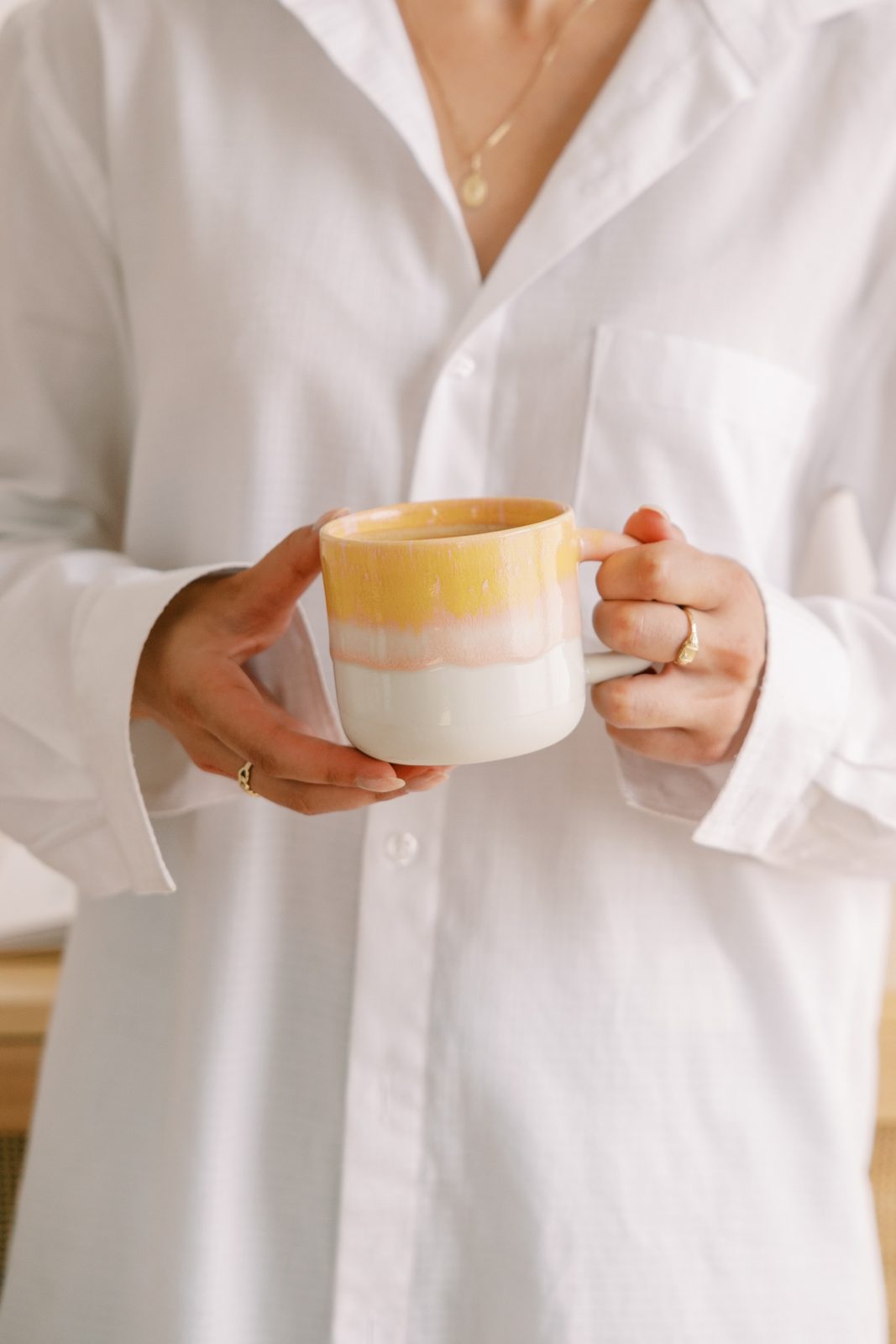 Hands holding a coffee mug, white shirt, gold necklace