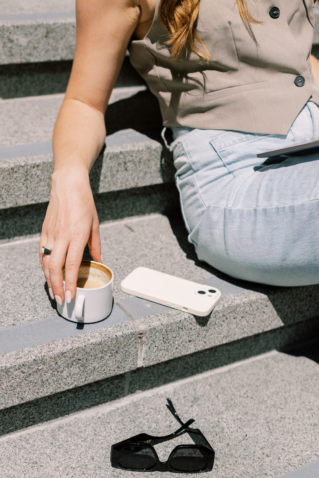 A salon owner sitting on sunny steps with a coffee, phone face down