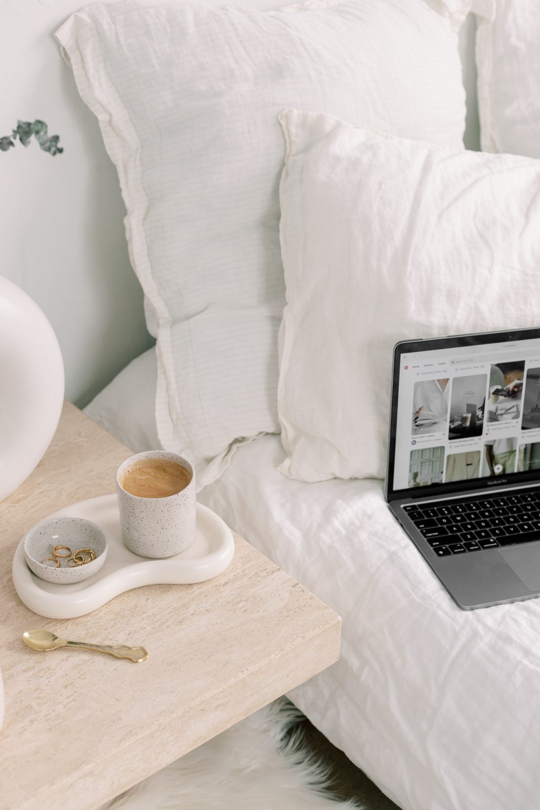 Coffee and an open laptop on a bedside table in morning light