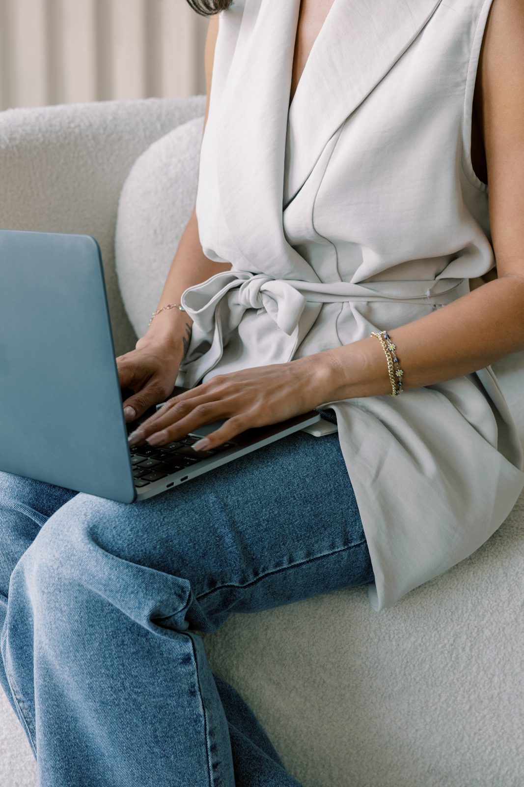 Hands typing on a laptop on a soft cream couch