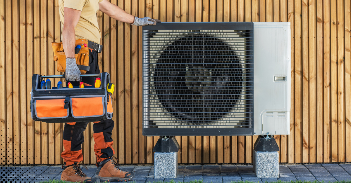Technician standing beside an outdoor heat pump system. Technician standing beside an outdoor heat pump system.