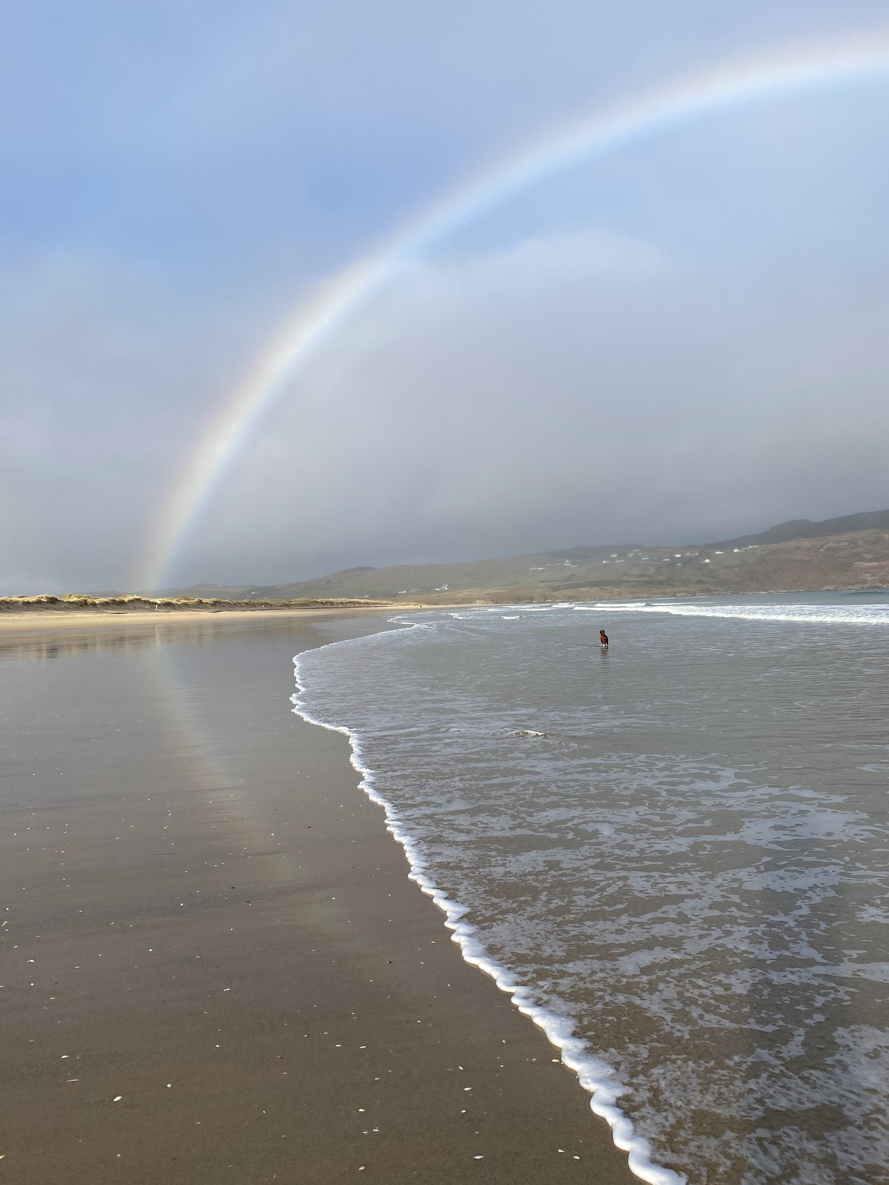 A rainbow arcing over a quiet Donegal beach at the water's edge