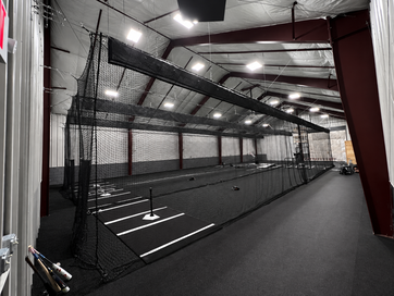 Batting cage training facility inside a metal building with turf floors and netting